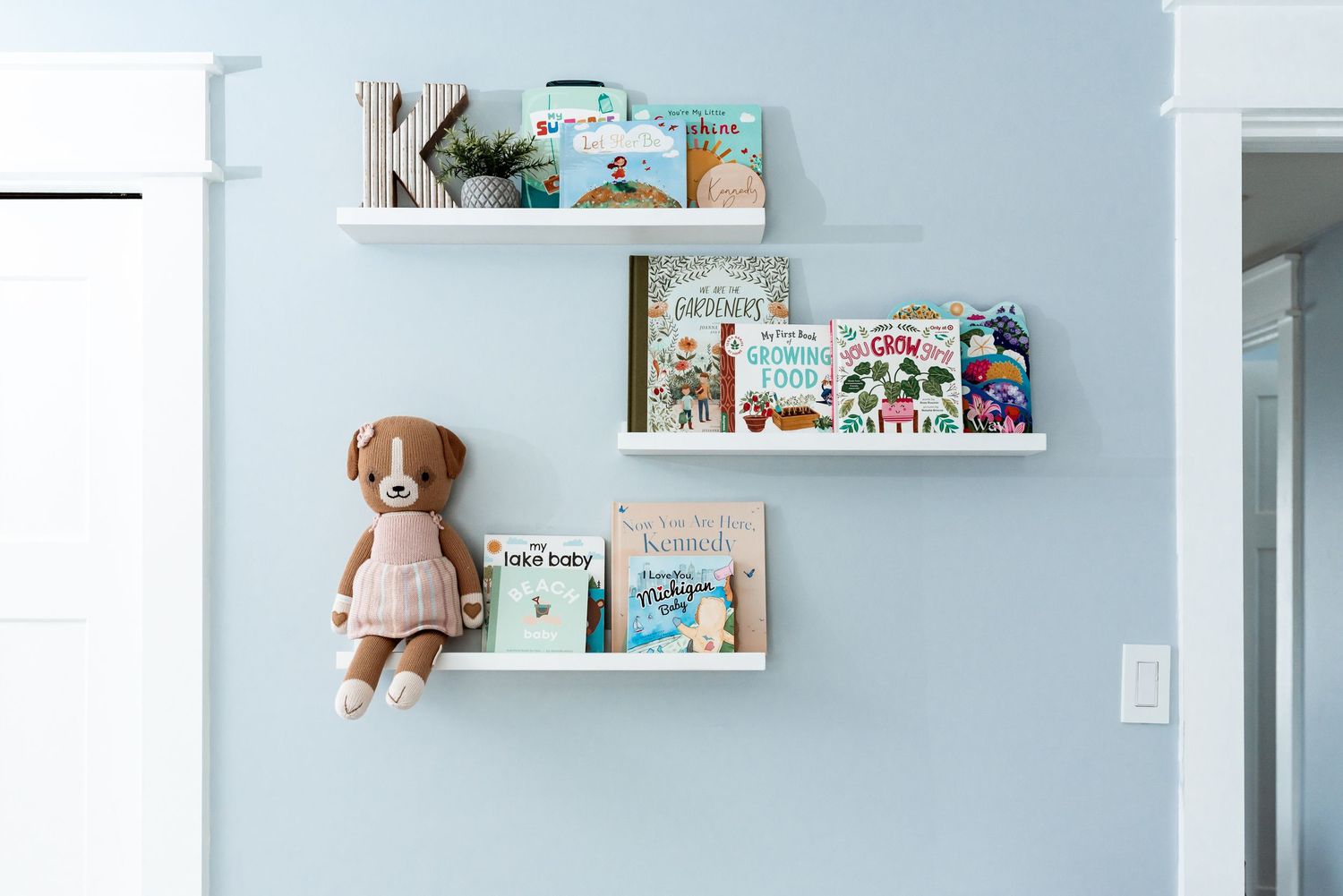 White floating shelves displaying children's books and a plush stuffed animal against a light blue wall.