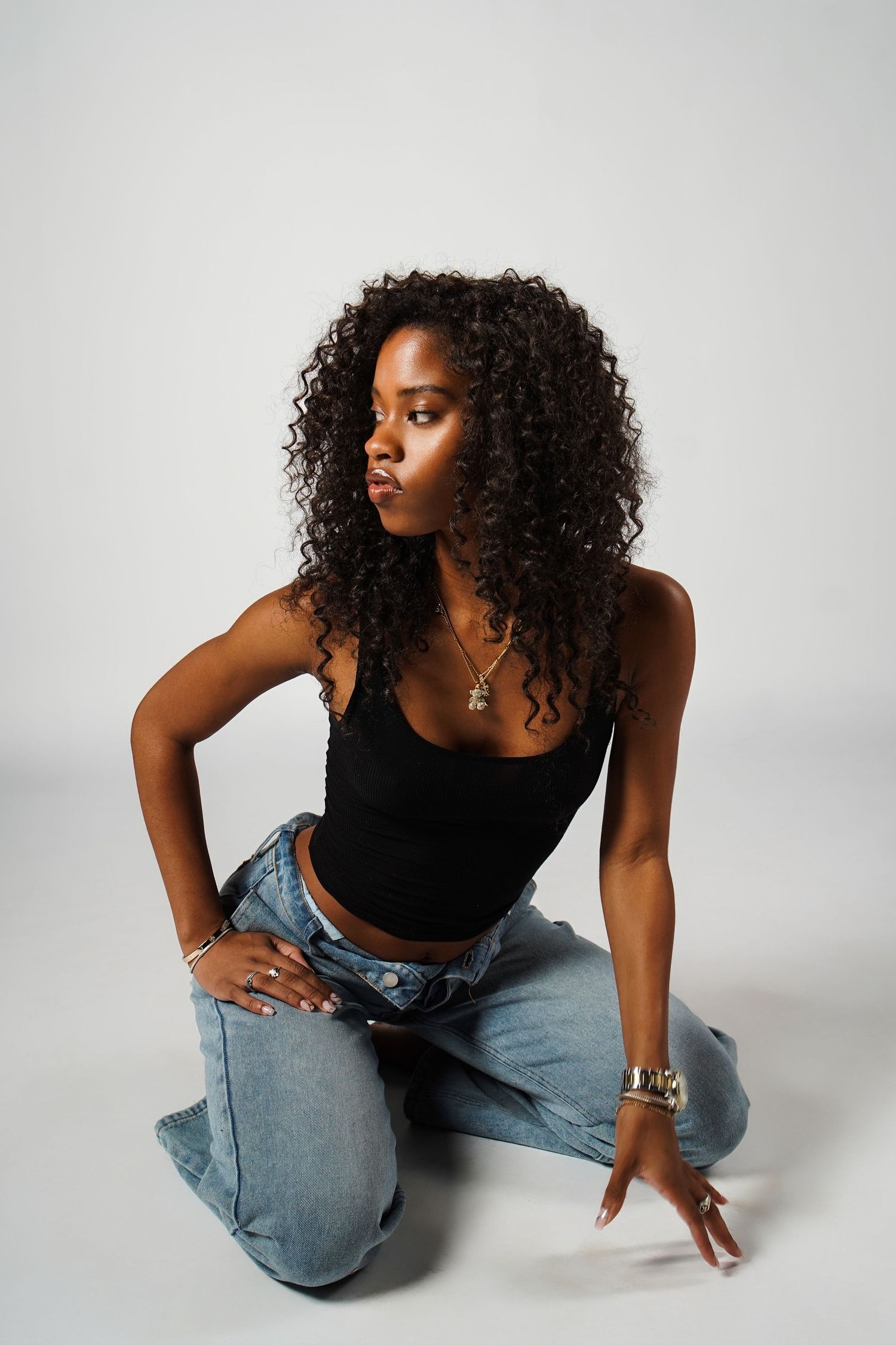 Model in black top and jeans poses gracefully in studio against white background showing different angles.