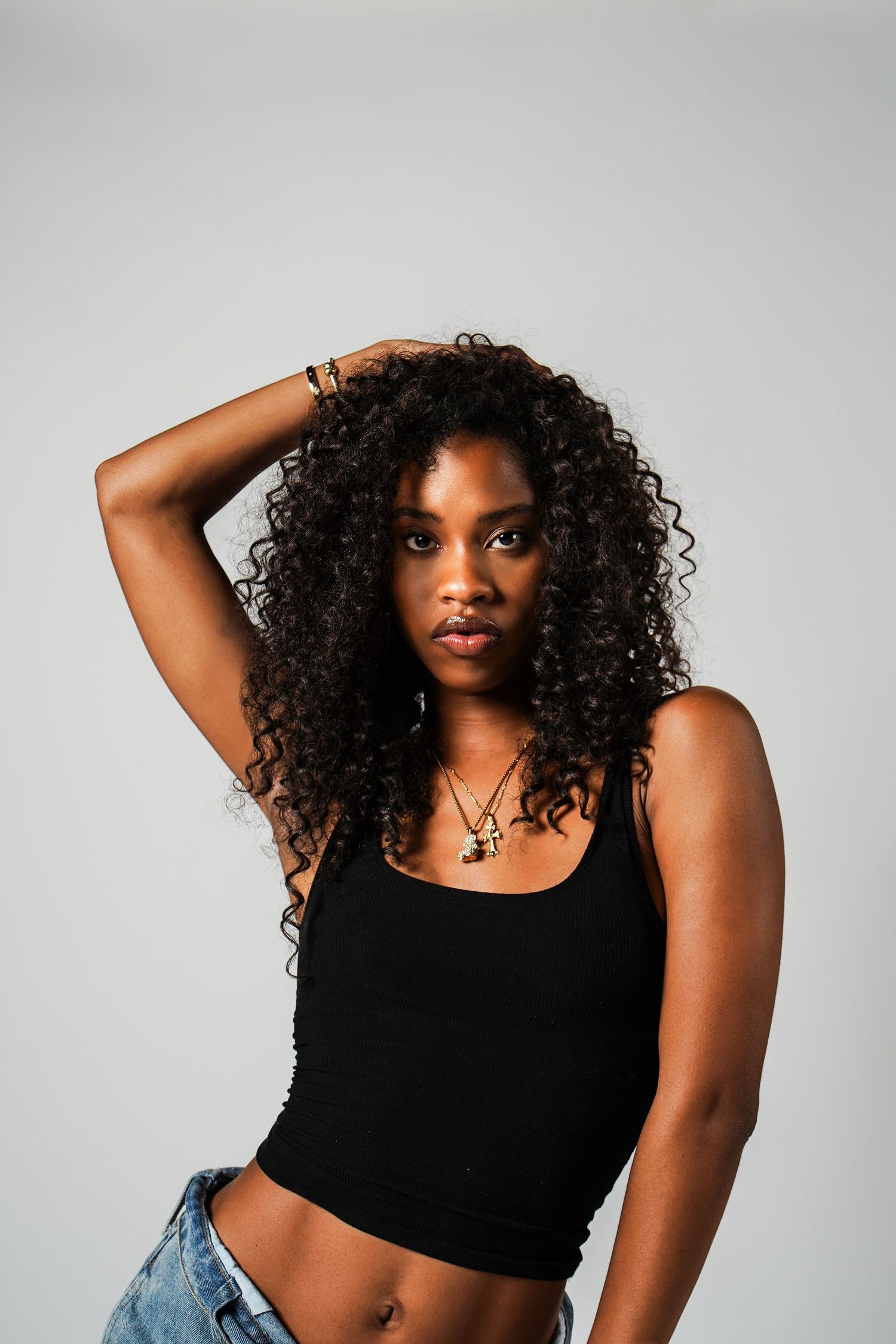 A model in a black crop top and denim poses against a light gray background in three artistic shots.