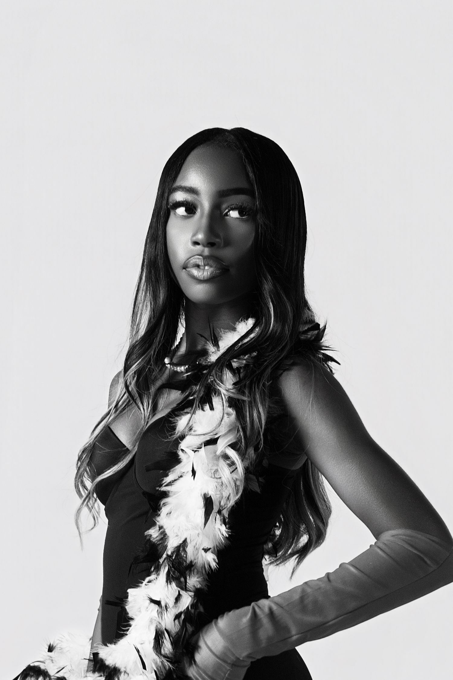 A black and white fashion portrait series showing dynamic poses in a white feathered dress against a light background.