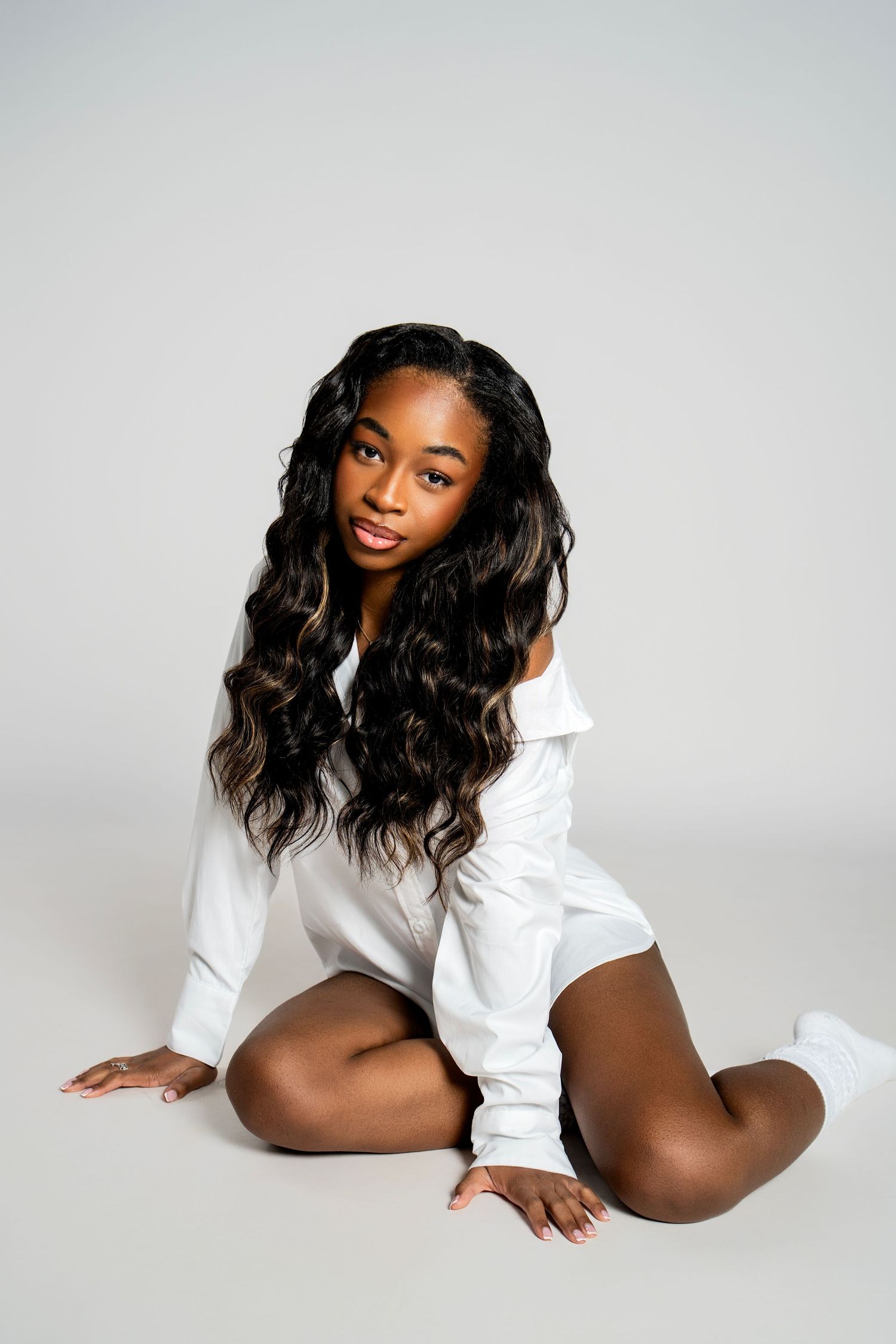 Artistic boudoir photo series showing a model in a white button-down shirt posing gracefully against light backdrop.