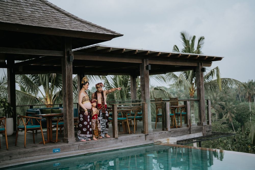 A luxury resort swimming pool with thatched roof buildings and palm trees in a tropical setting.
