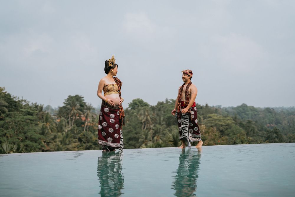 People enjoying an infinity pool overlooking a scenic tropical landscape with mountains in the distance.