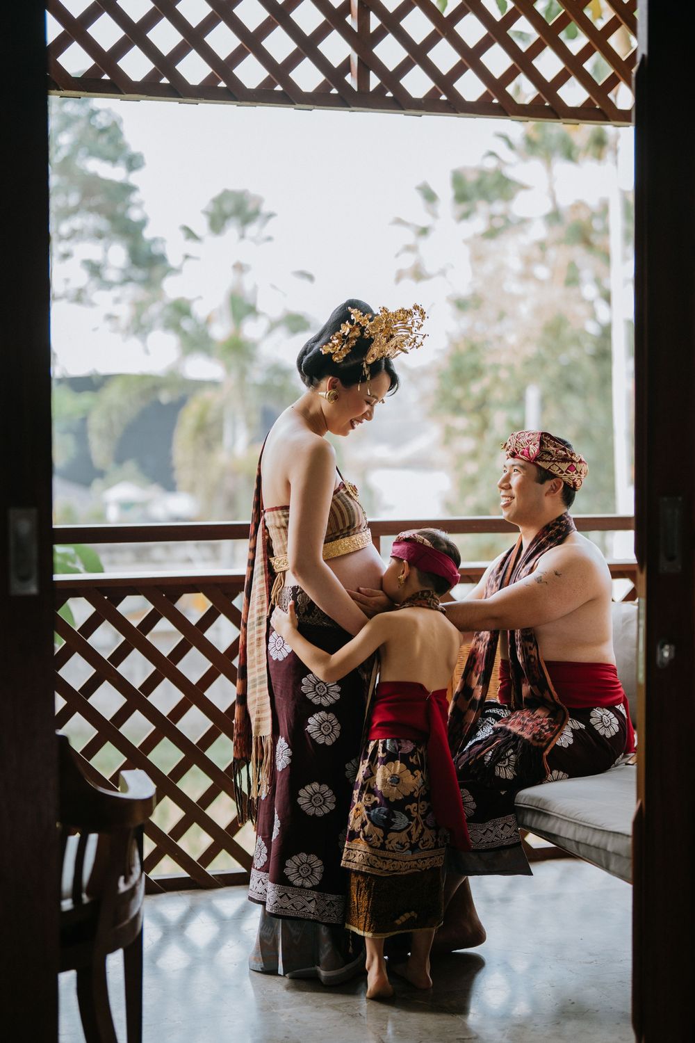 People in traditional Balinese attire relaxing on a covered patio with lattice walls.