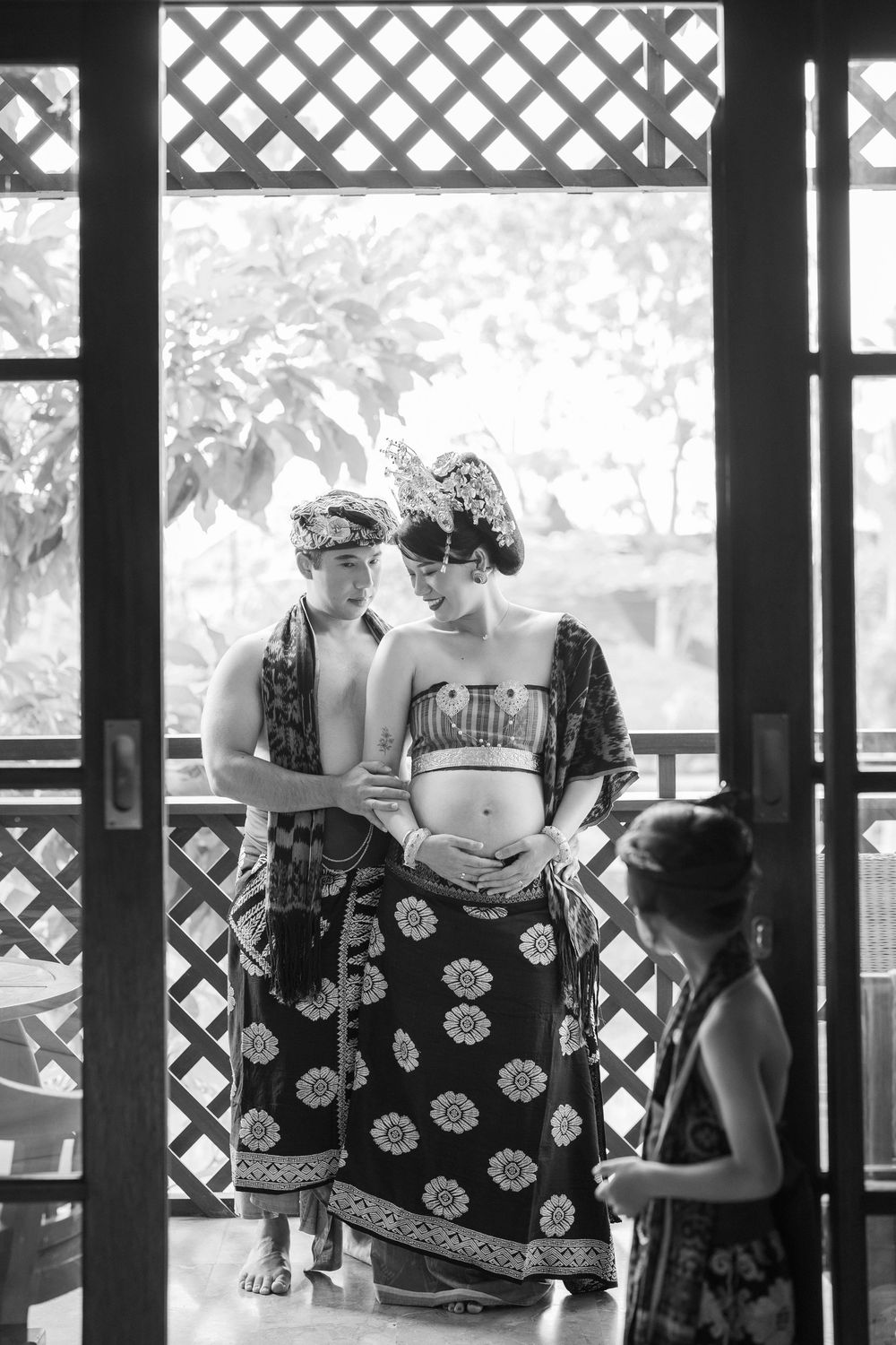 Black and white photo of people in traditional clothing sitting in a covered pavilion with lattice walls.