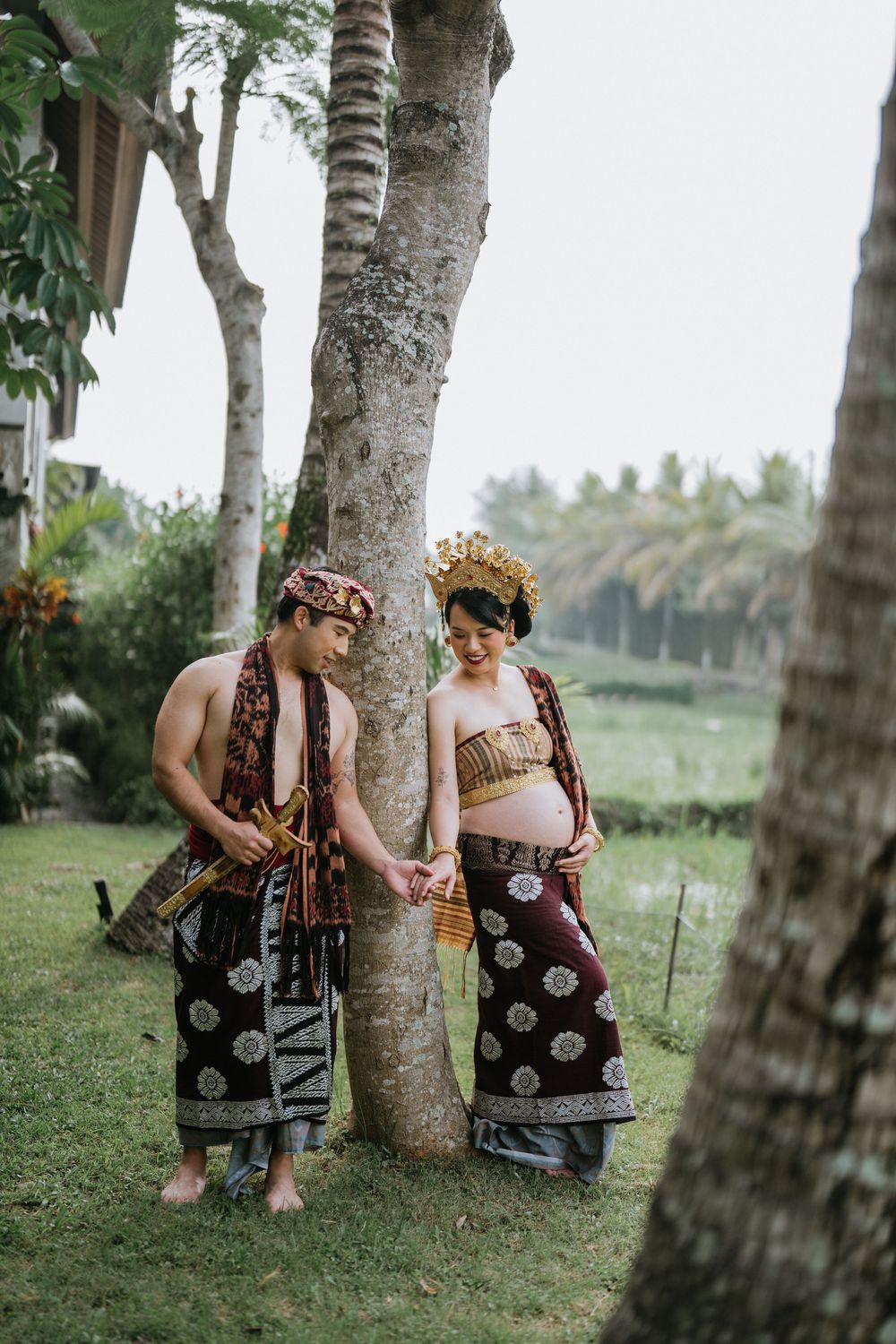 Two people in traditional dress sitting among palm trees in a lush tropical garden.
