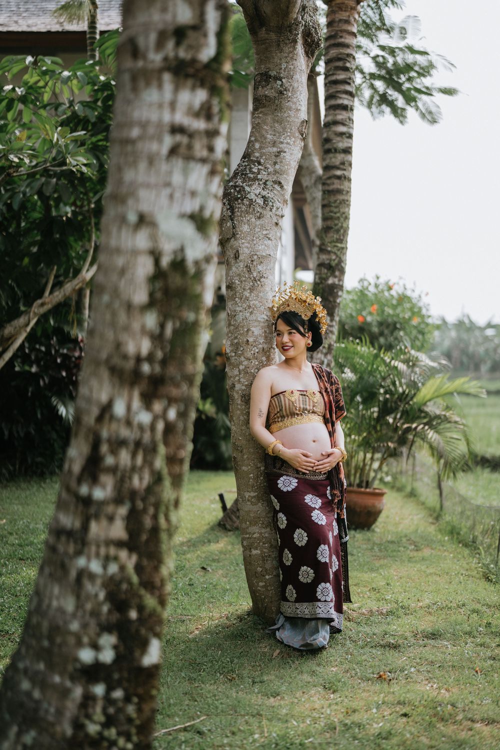 Person in traditional Balinese dress posing among palm trees in a tropical garden.