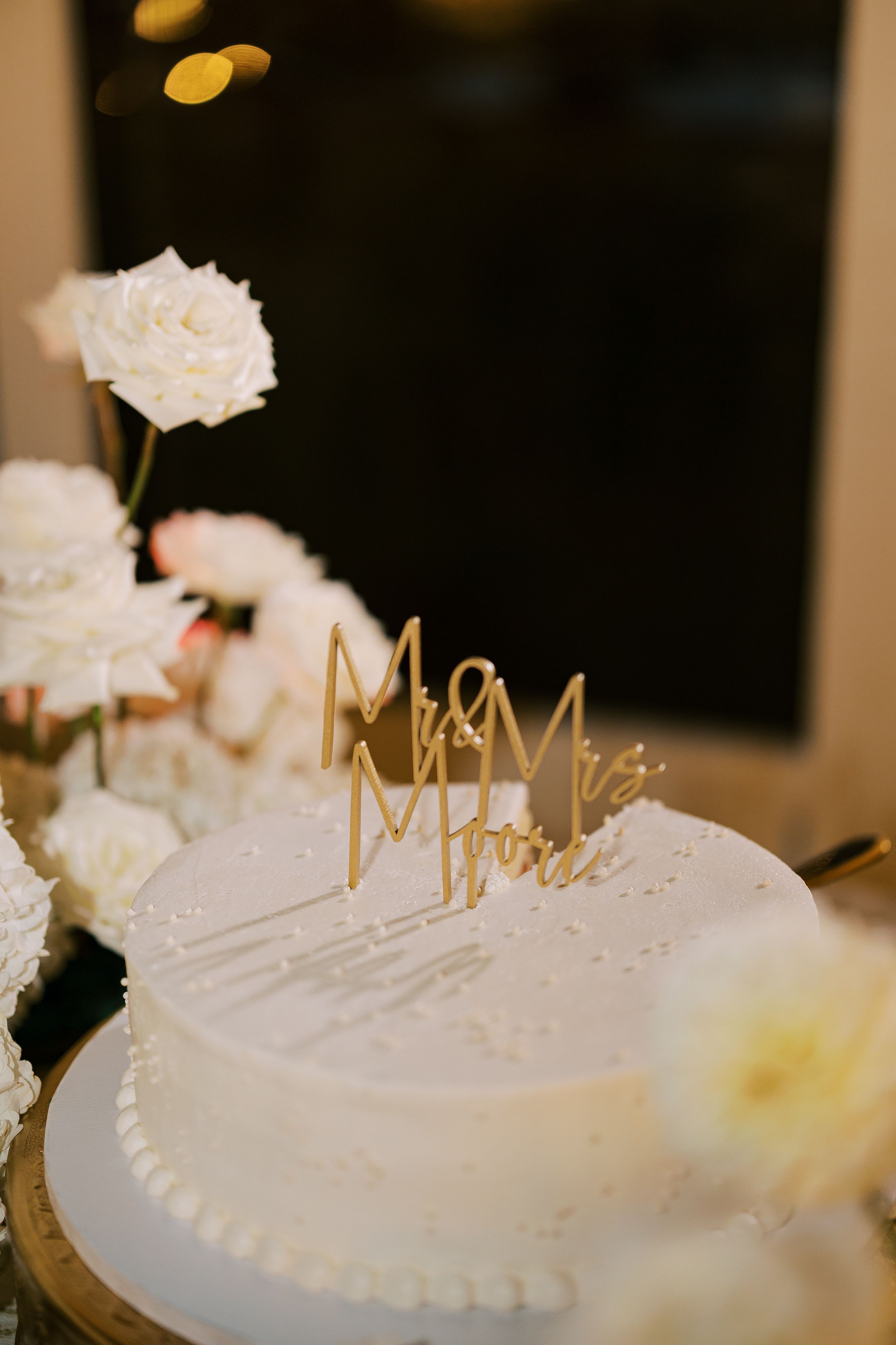 Elegant white wedding cake with delicate icing details and golden crown decorations on top.