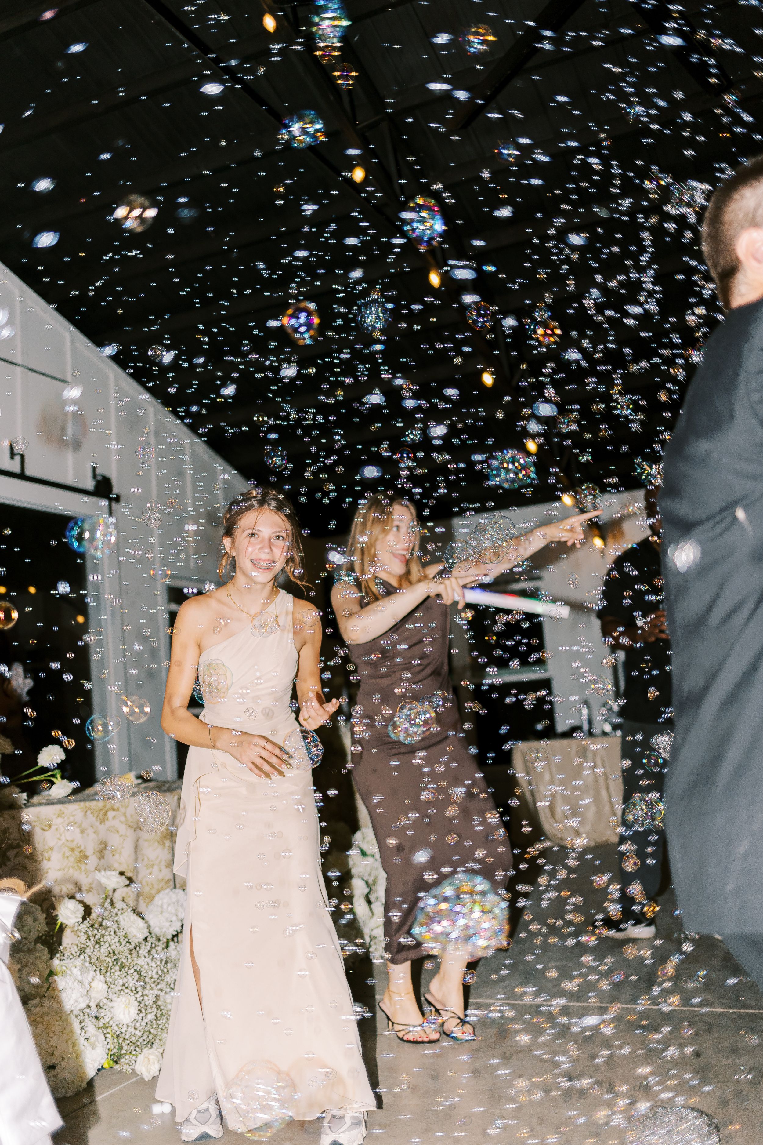 Wedding celebration with guests dancing amid falling confetti in an illuminated nighttime setting.
