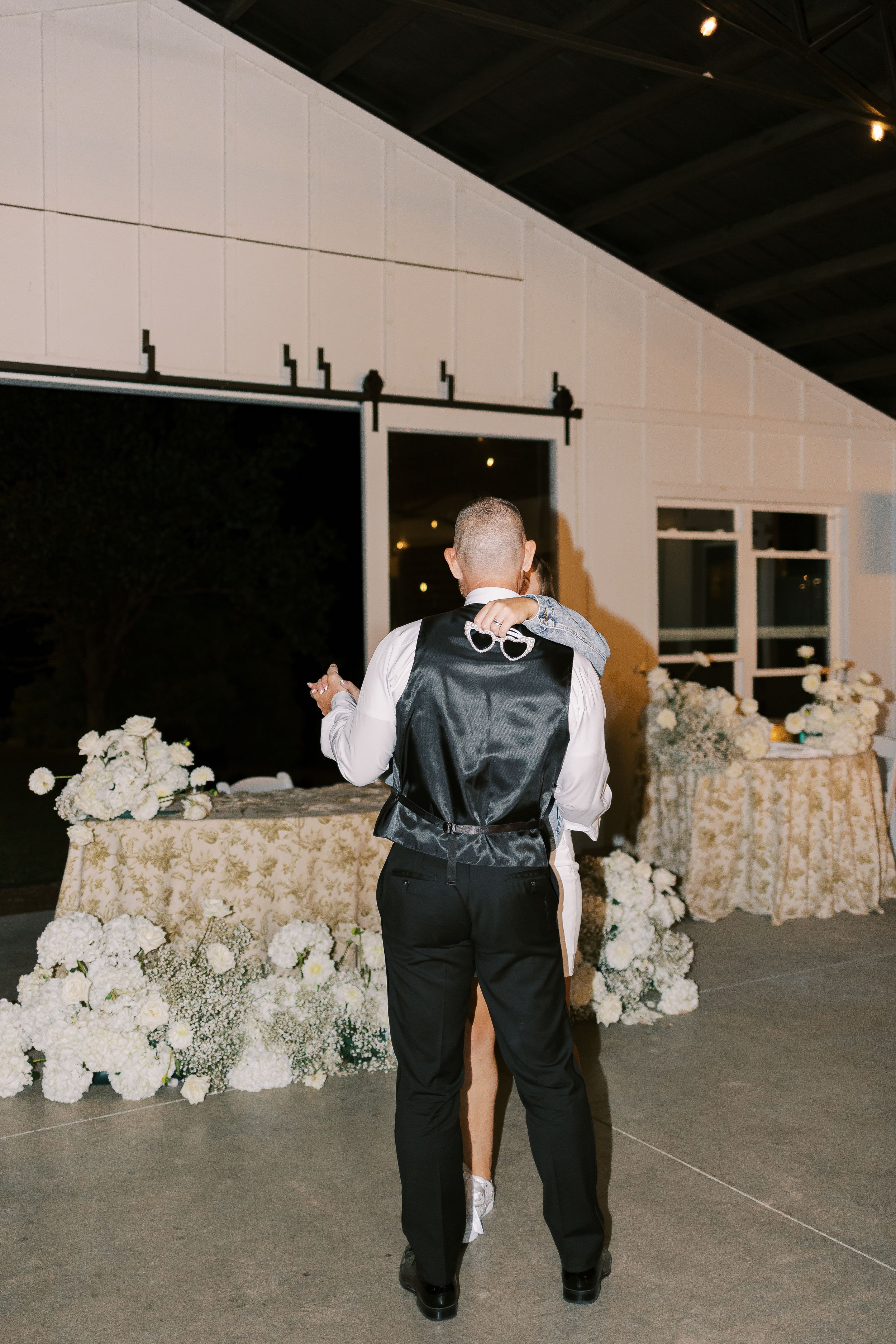 Server in black vest and white shirt moves across empty dance floor with white floral arrangements visible along the wall.