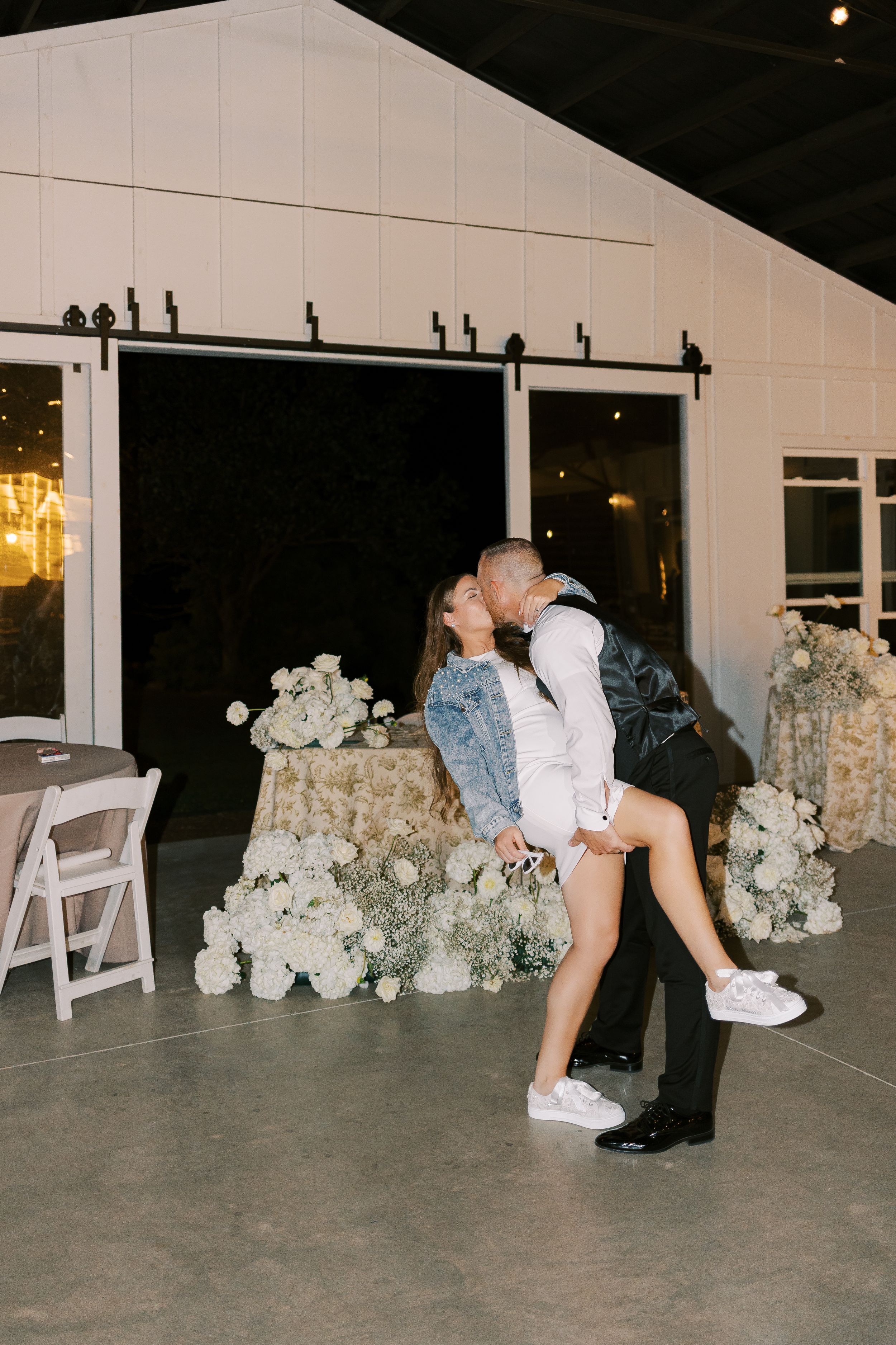 Wedding party celebrations in front of a white venue with floral decorations at night.