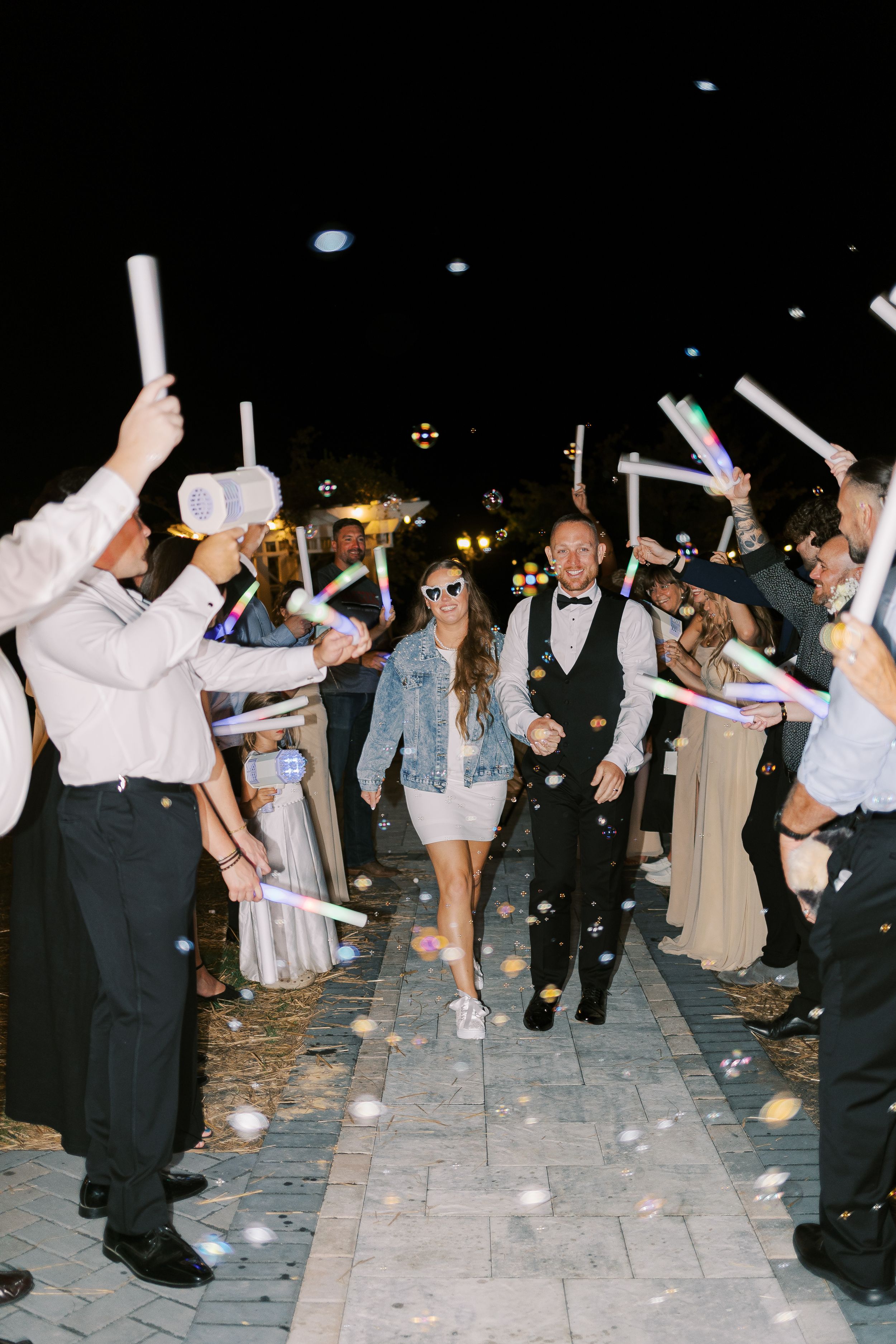 Wedding guests celebrating with light-up foam batons during an evening outdoor reception.
