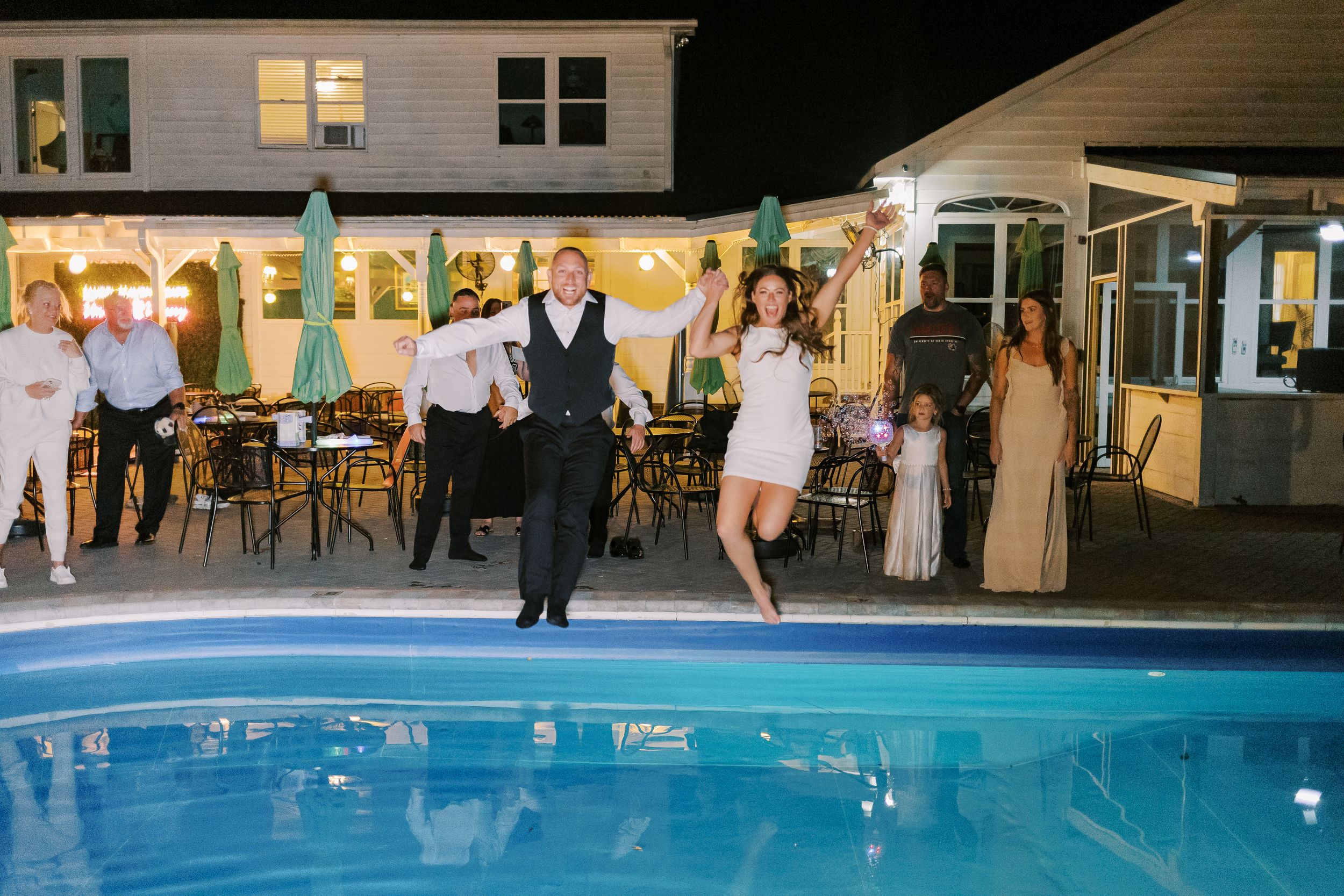 Outdoor wedding reception venue at night with illuminated swimming pool and string lights.