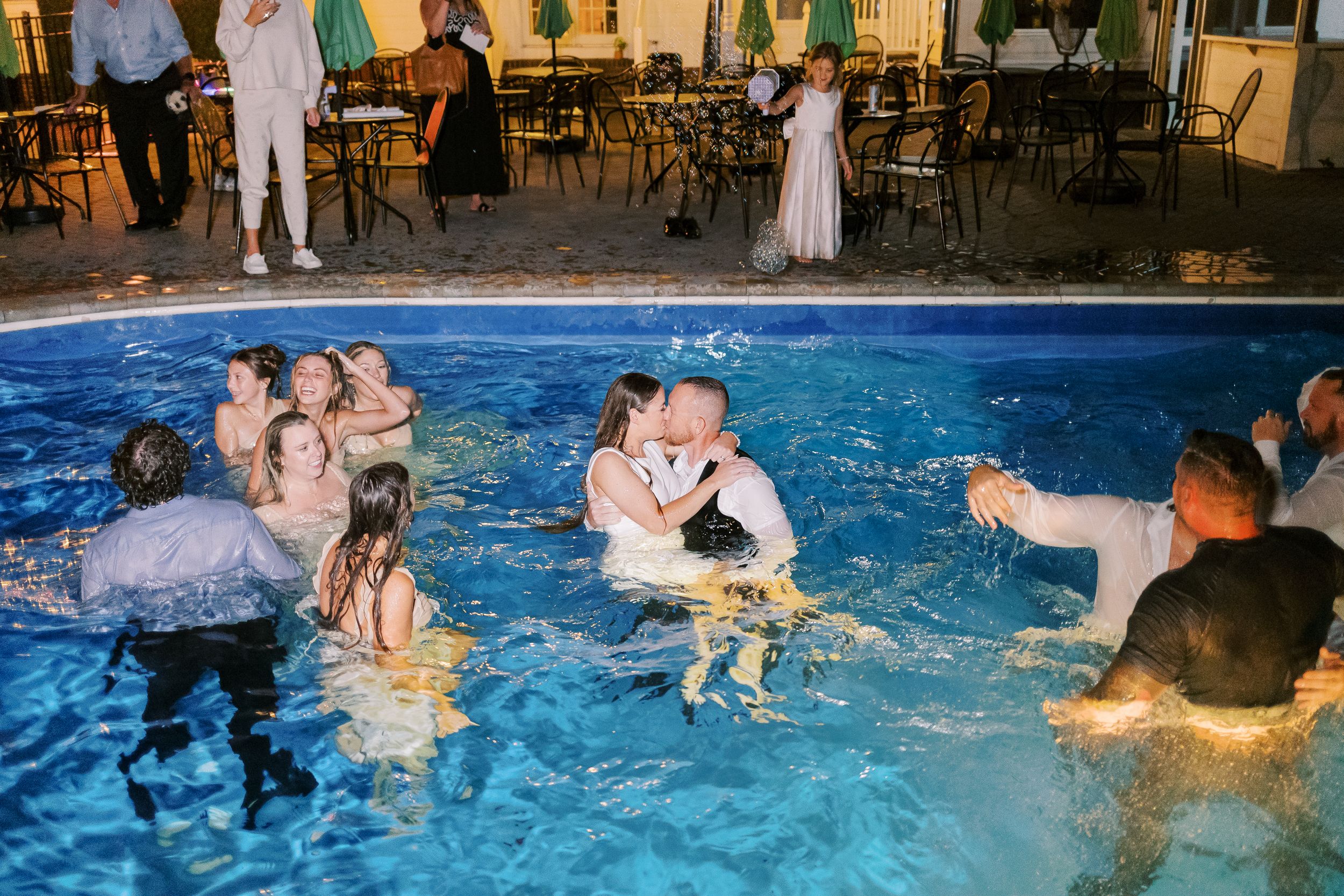 Wedding guests enjoying a nighttime pool party celebration with playful splashing and swimming.