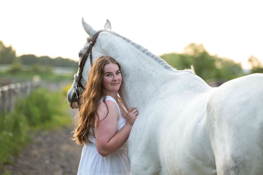 White horse and rider in golden sunlight stand gracefully in a dreamy outdoor setting at sunset.