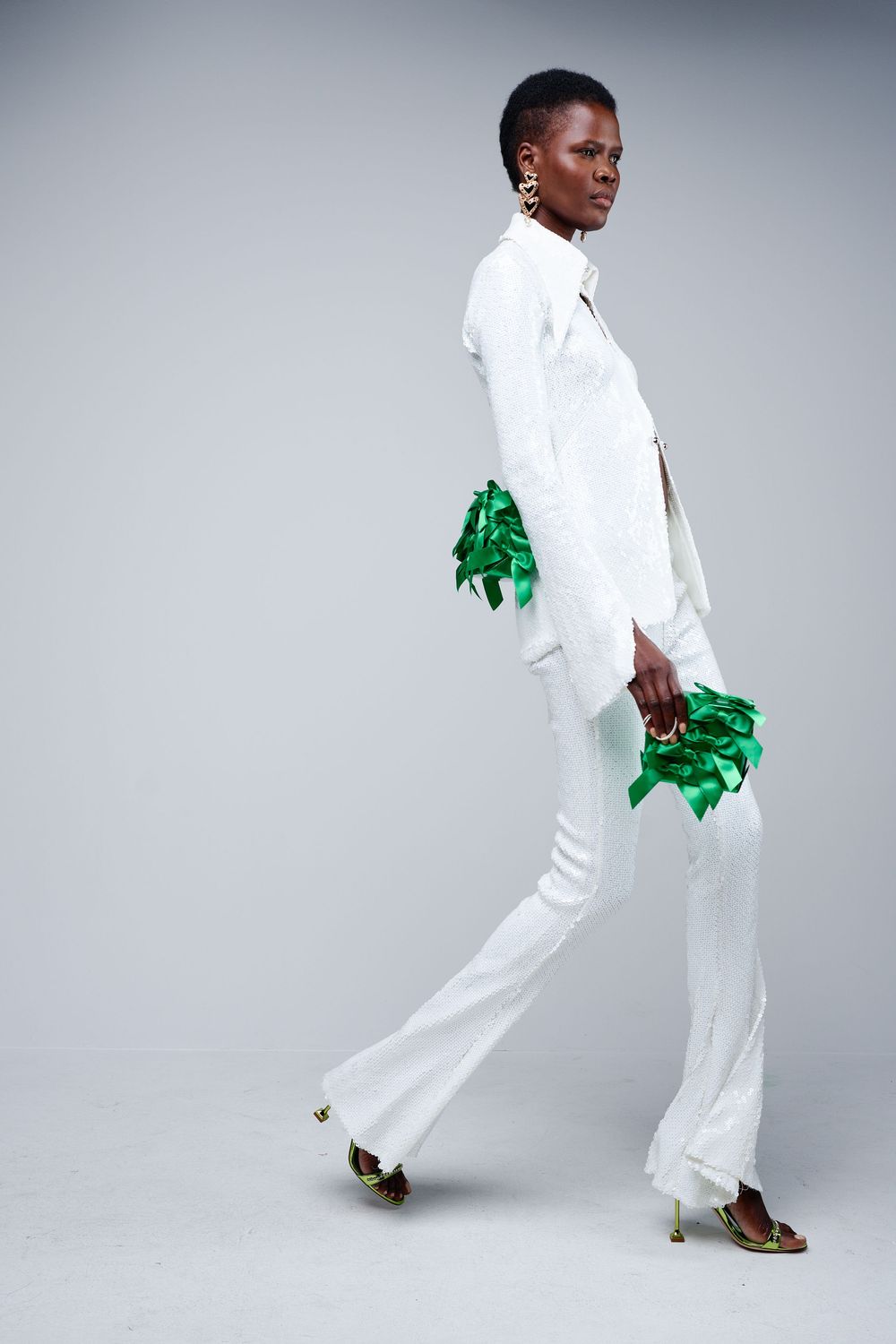 Person in crisp white outfit holds bright green prop while posing dynamically against gray background.