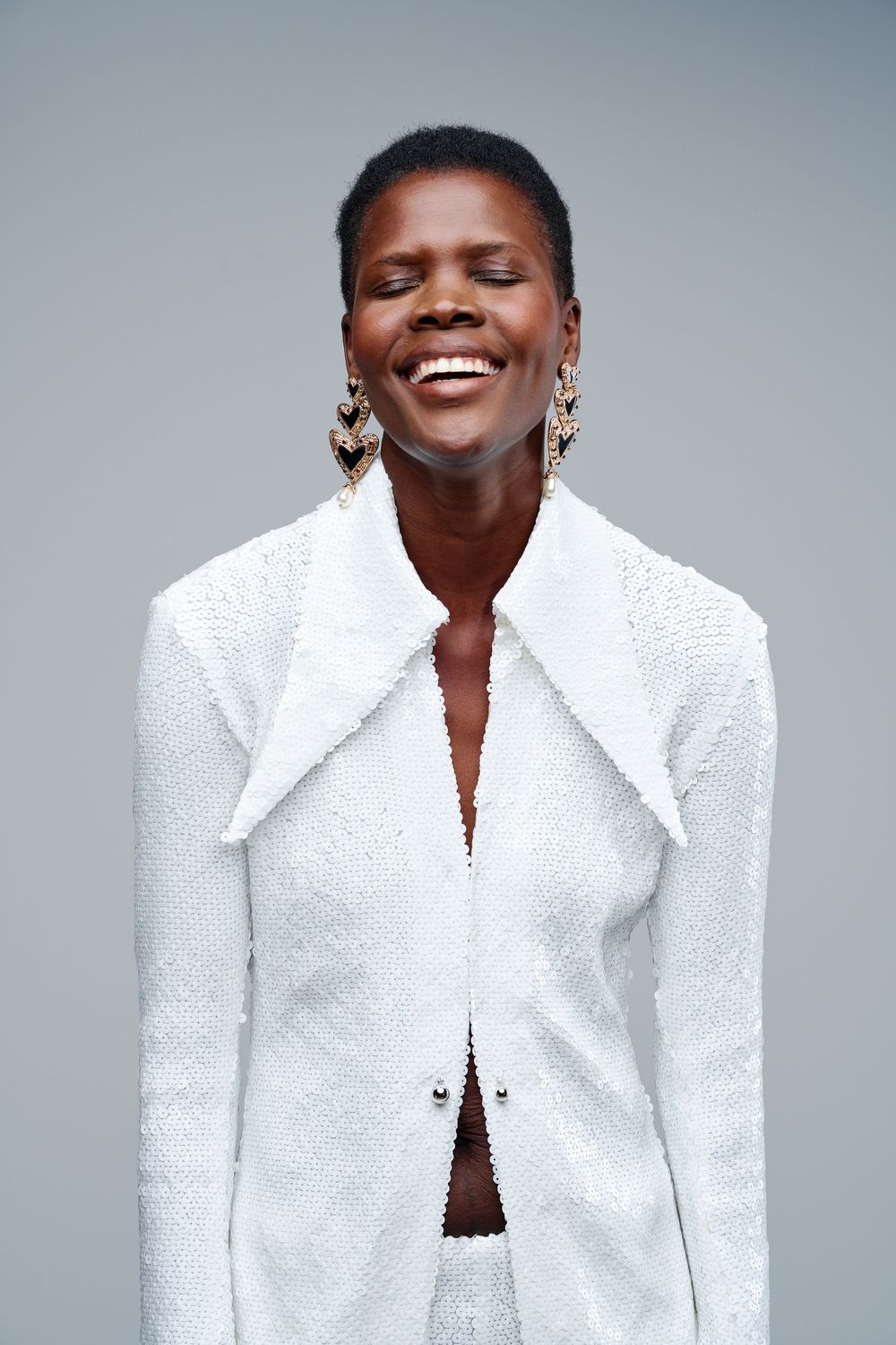 Fashion photo series showing a model in a textured white blazer jacket expressing joy against a gray background.