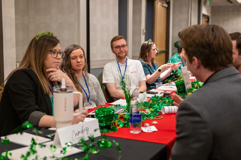 People gathered around a table for a networking event with festive green decorations visible in the background.