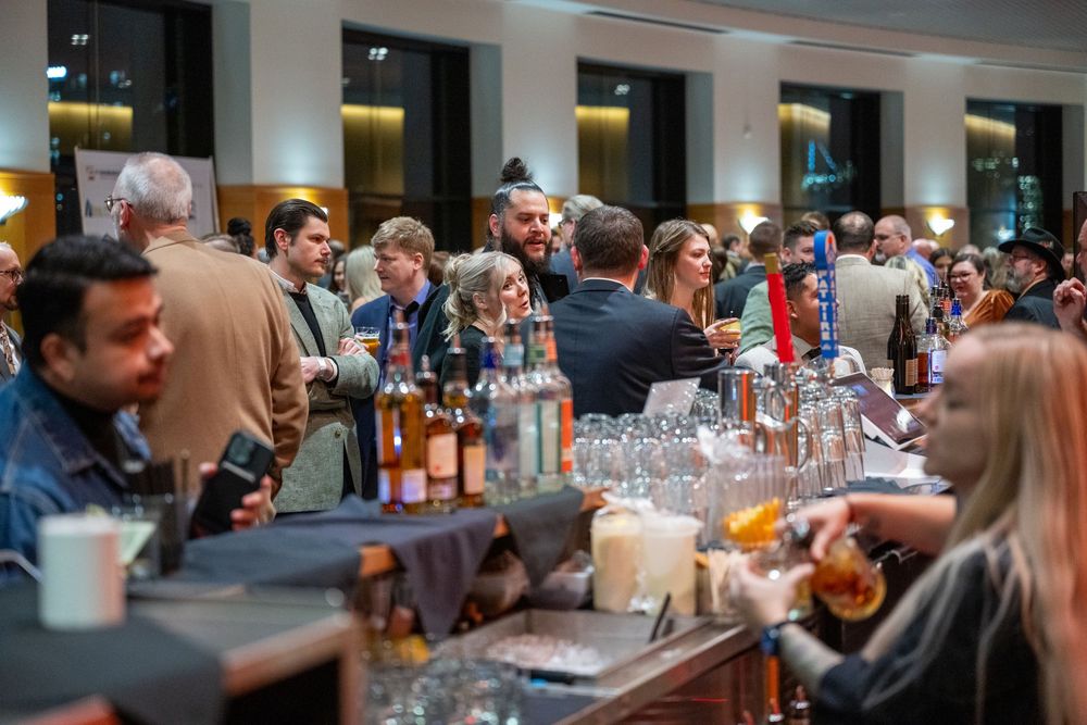 Patrons gathered at a crowded restaurant bar socialize and enjoy drinks together in a modern dining setting.