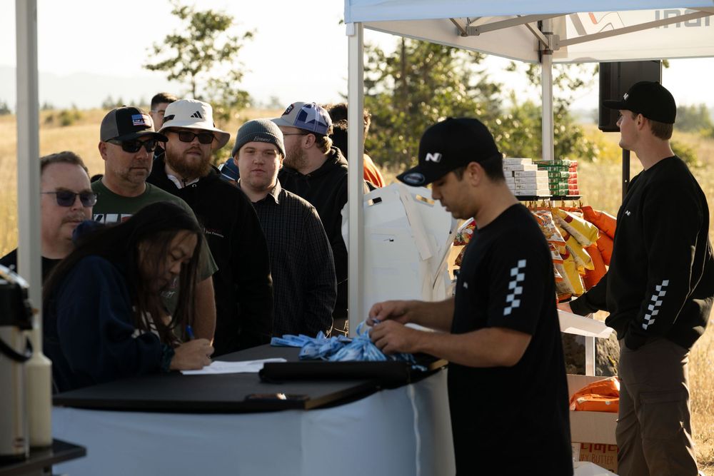 A group of people at an outdoor event standing around talking while wearing black and white clothing.