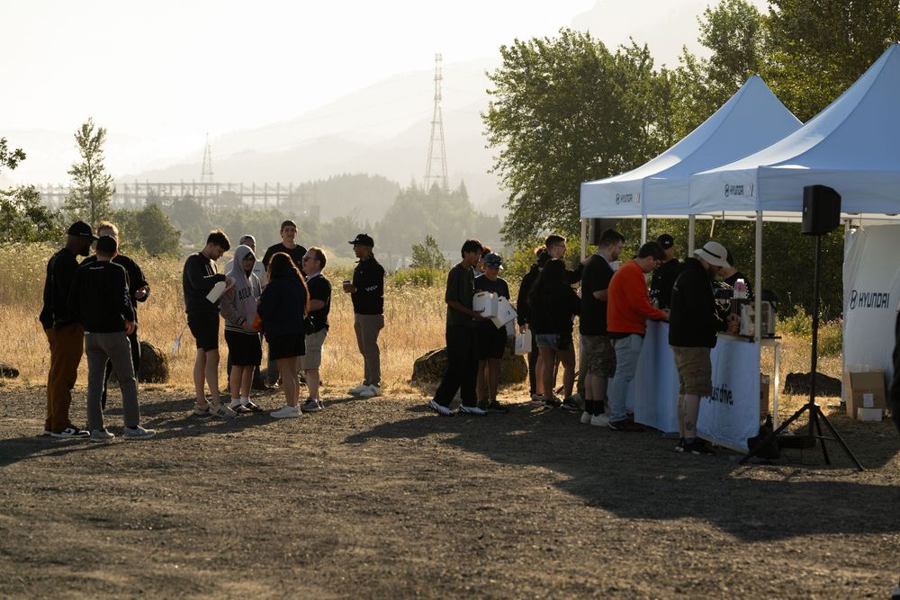 Silhouettes of people gathered at outdoor tents during a smoky or misty sunset event.
