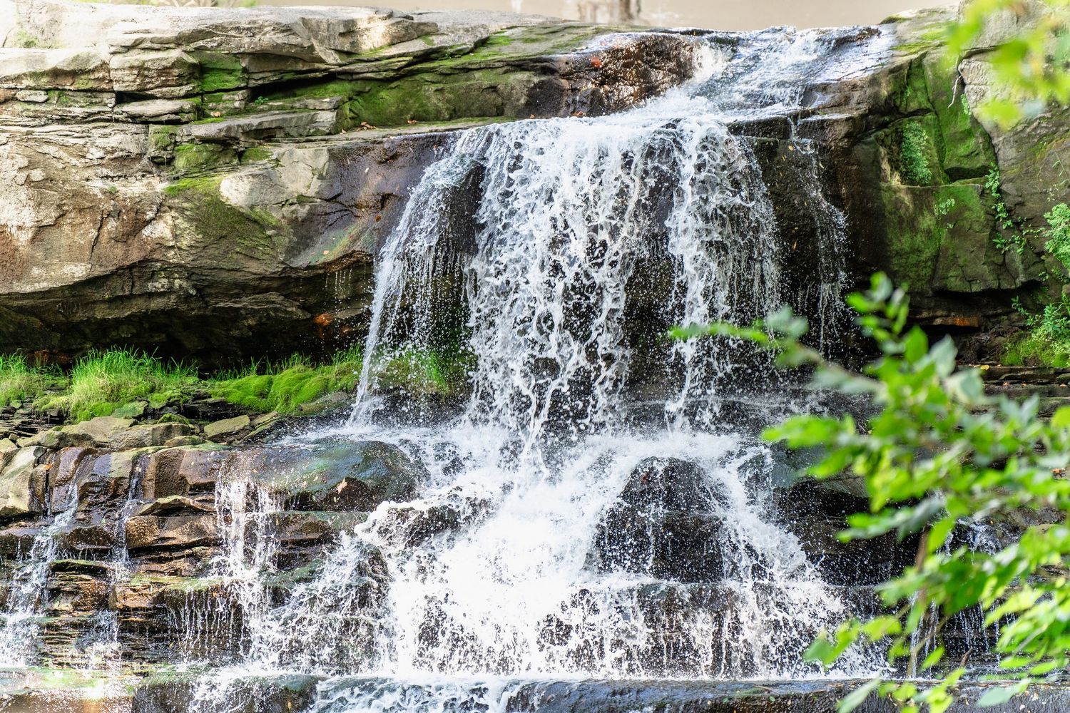 A cascading waterfall flows over multiple rocky ledges surrounded by lush green foliage in a state park setting at Brandywine Falls