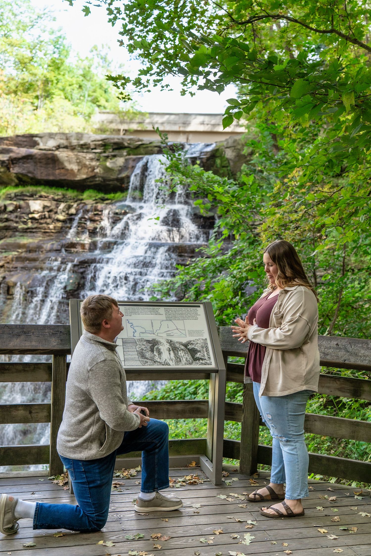 Couple getting engaged at scenic Brandywine falls overlook on wooden viewing platform for surprise engagement photo session