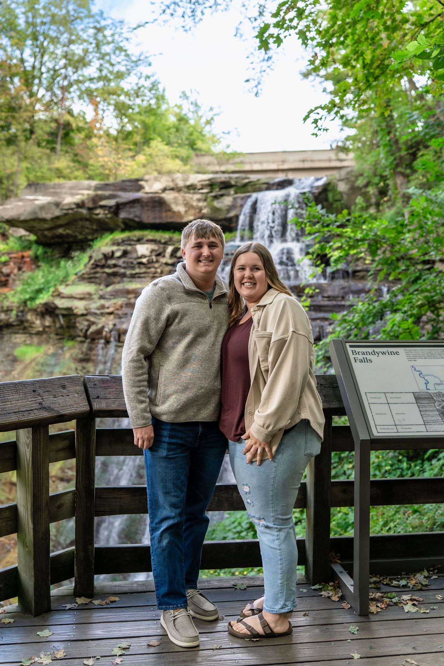 Newly engaged couple sharing intimate moment on wooden observation deck with Brandywine Falls in Ohio for surprise engagement photos
