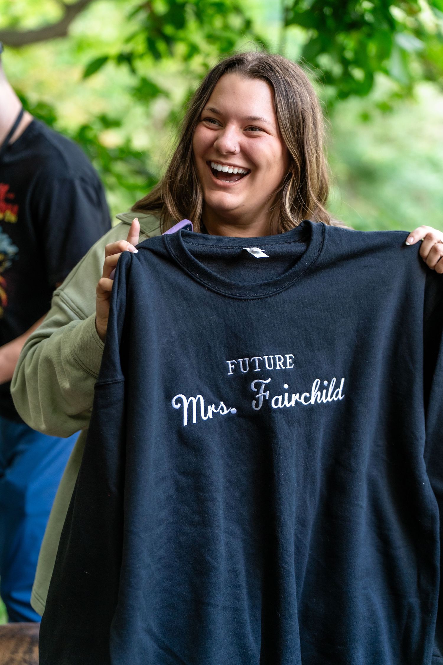 Person joyfully displaying a navy sweatshirt with Mrs. Fairchild text against Brandywine Falls in Ohio for surprise engagement session