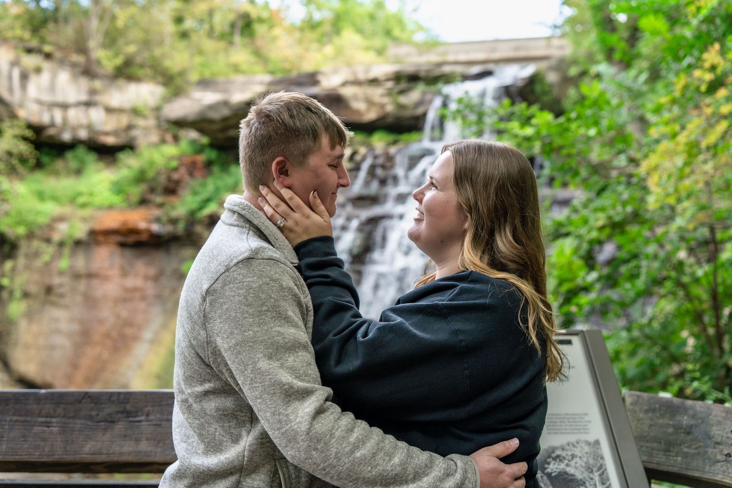 Couple embracing in romantic engagement photoshoot with scenic natural backdrop at Brandywine Falls in Ohio during surprise engagement photo