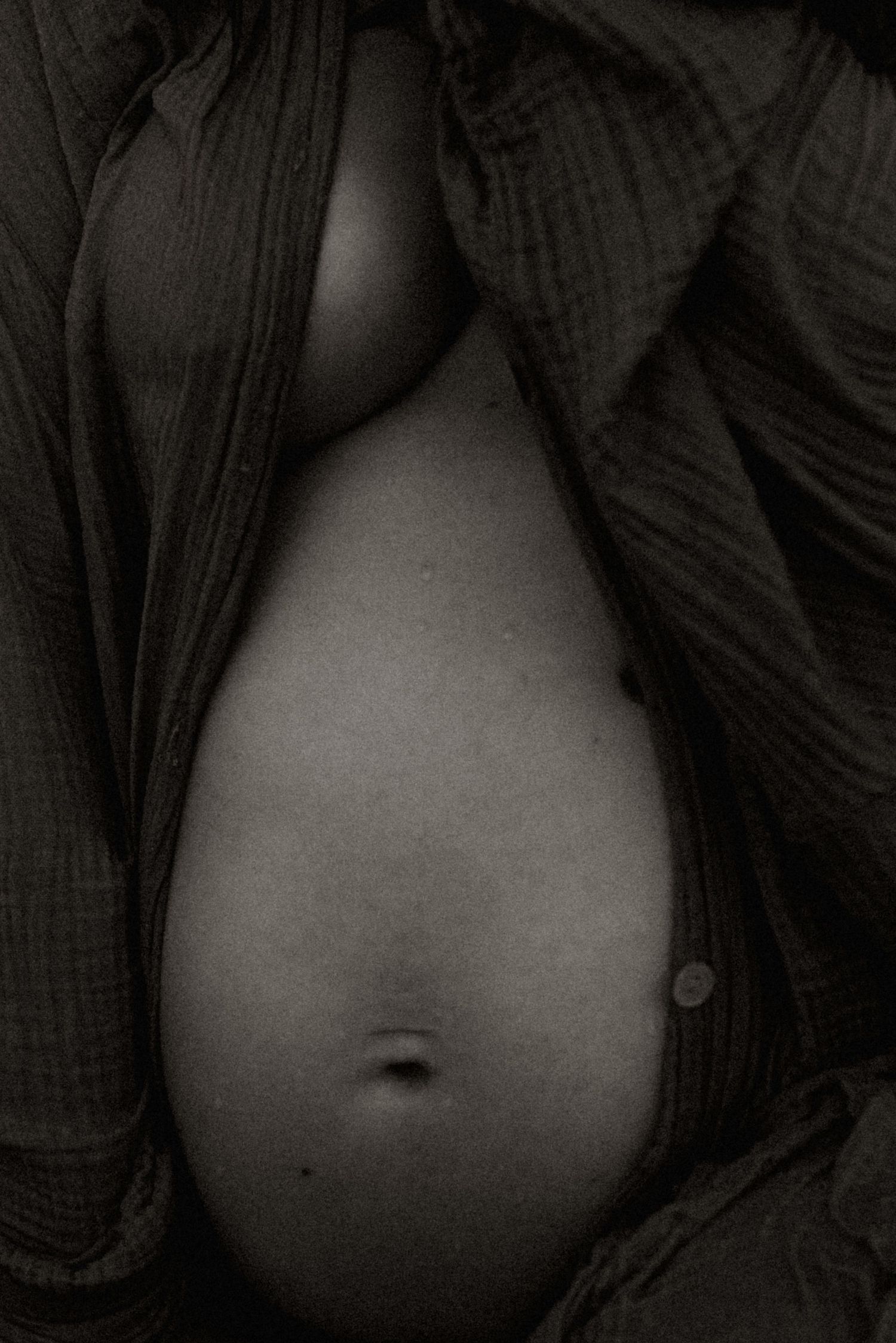 A black and white close-up in Javea photograph of an exposed pregnant belly surrounded by dark fabric. Javea maternity photographer