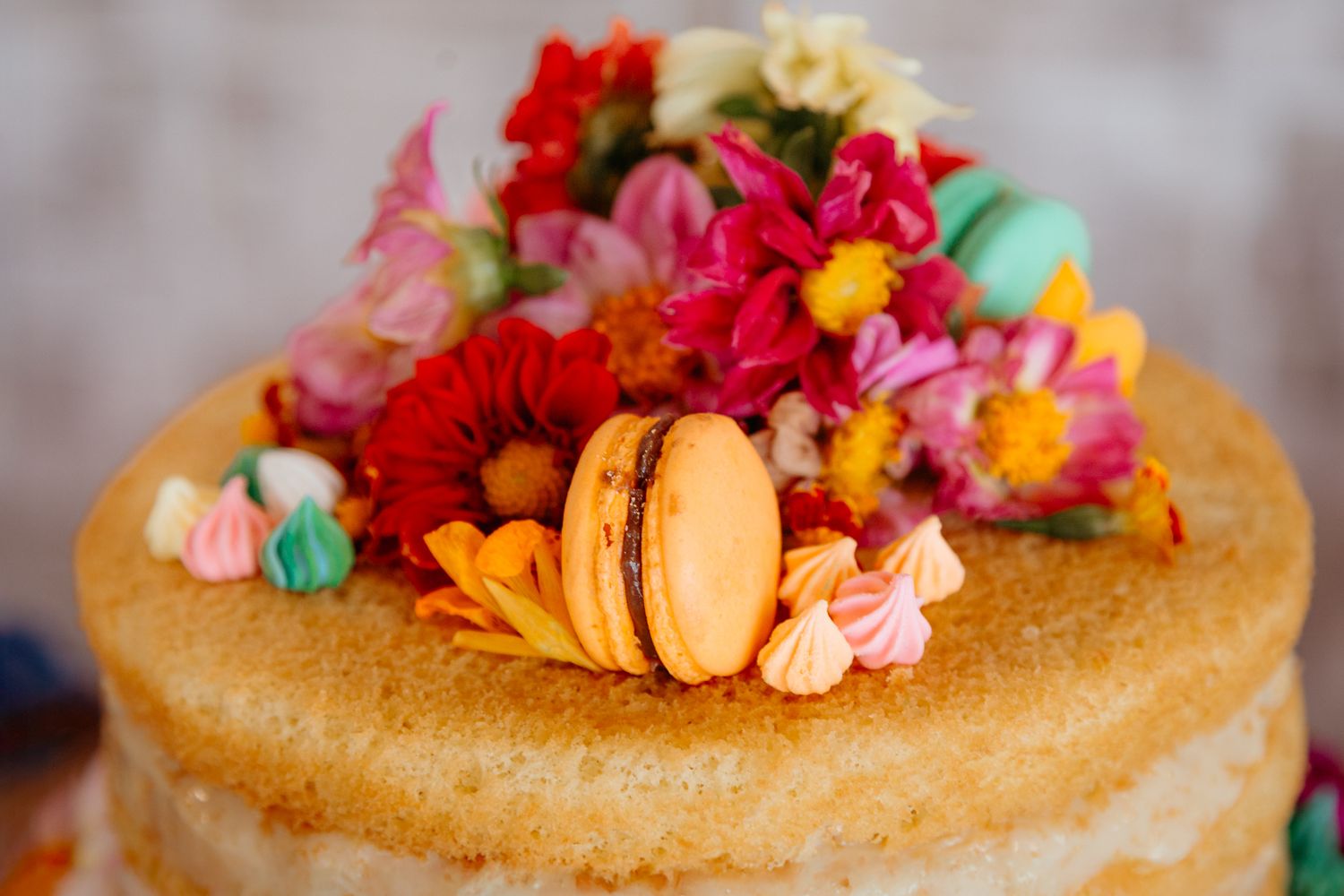 Naked cake decorated with vibrant flowers, macarons and colorful meringues on top in a close-up view.