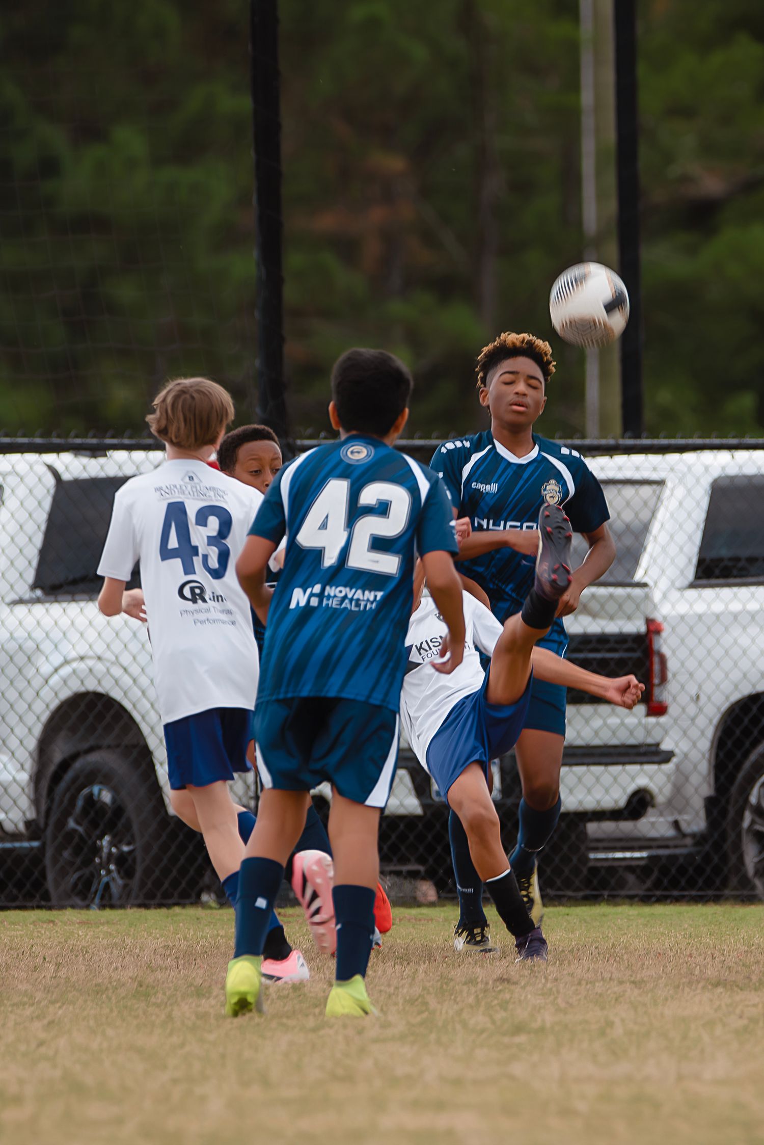 Youth soccer players practice heading drills on a grass field during team training session.
