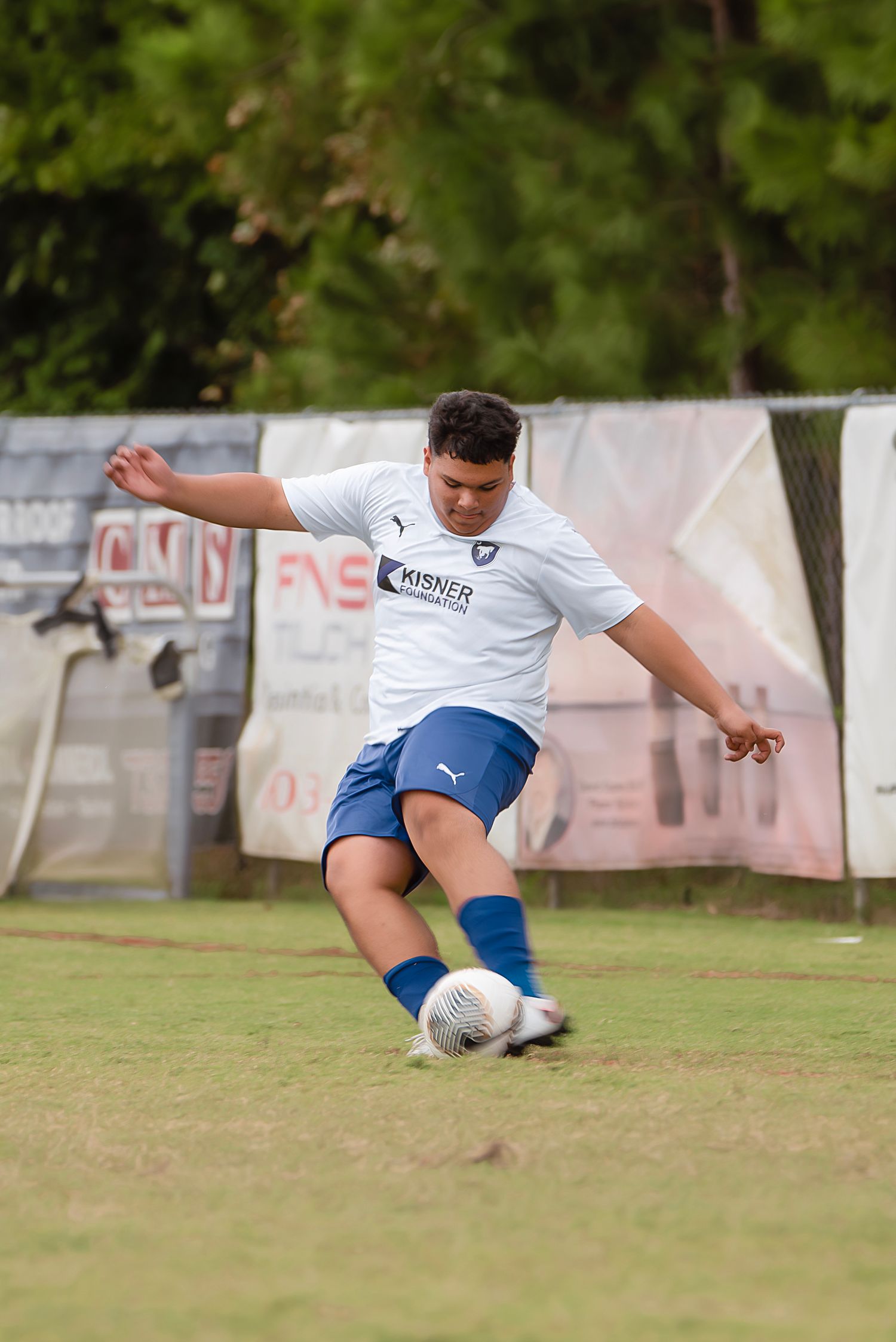 Soccer player in white jersey and blue shorts performs a kicking motion on grass field during match.