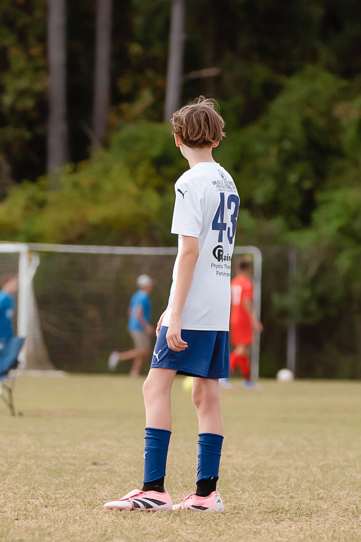 Young soccer players in white jerseys and blue pants stand on a grass field during a game.