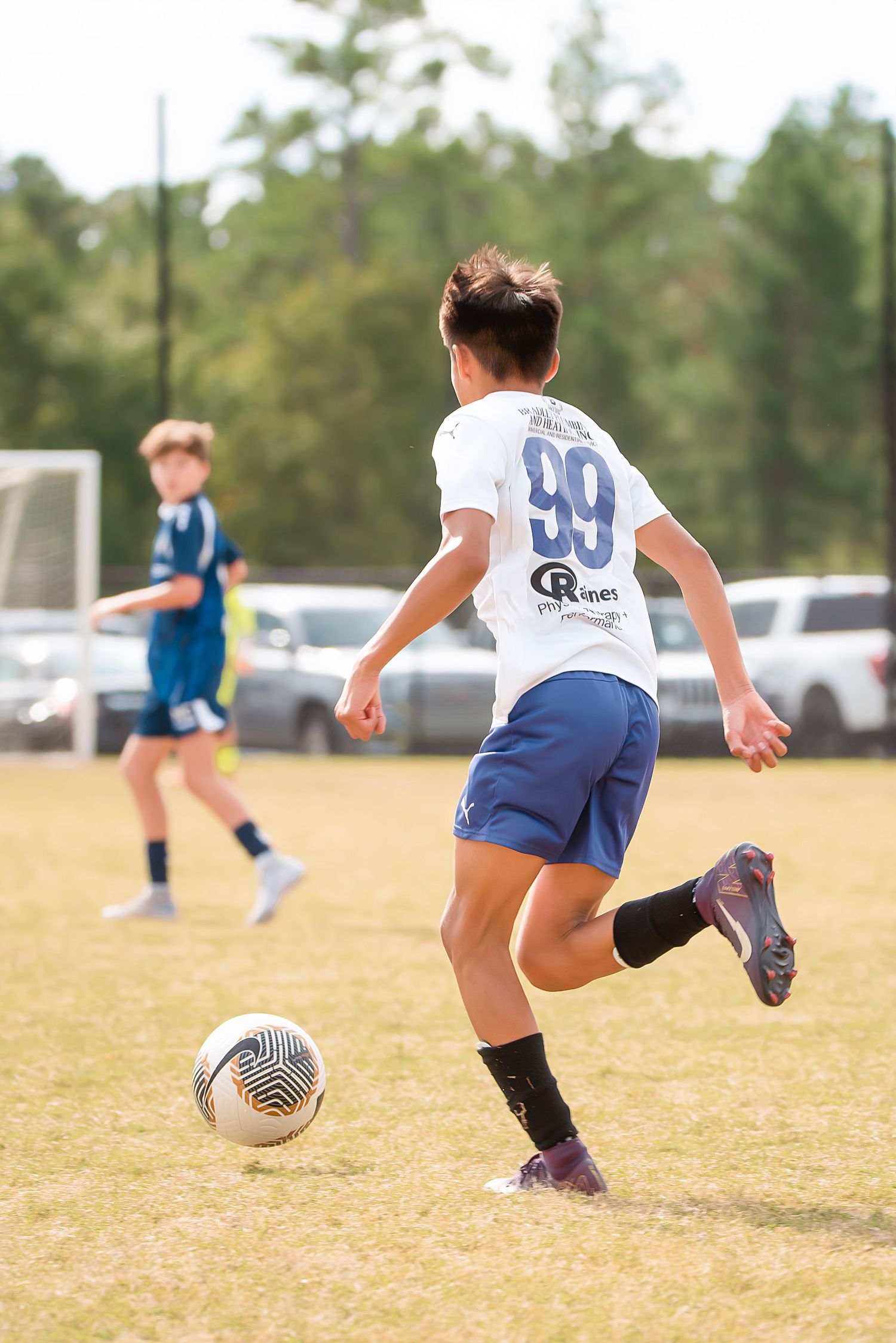 Soccer player in white jersey and blue shorts performs a kicking motion sequence on a grass field during practice.
