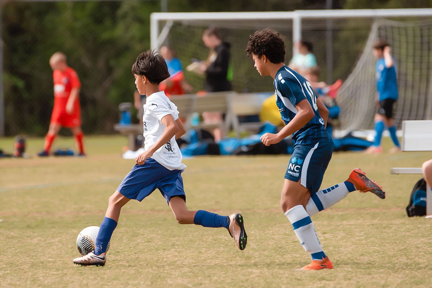 Soccer player in blue uniform performing a sliding tackle motion on grass field during daytime match.