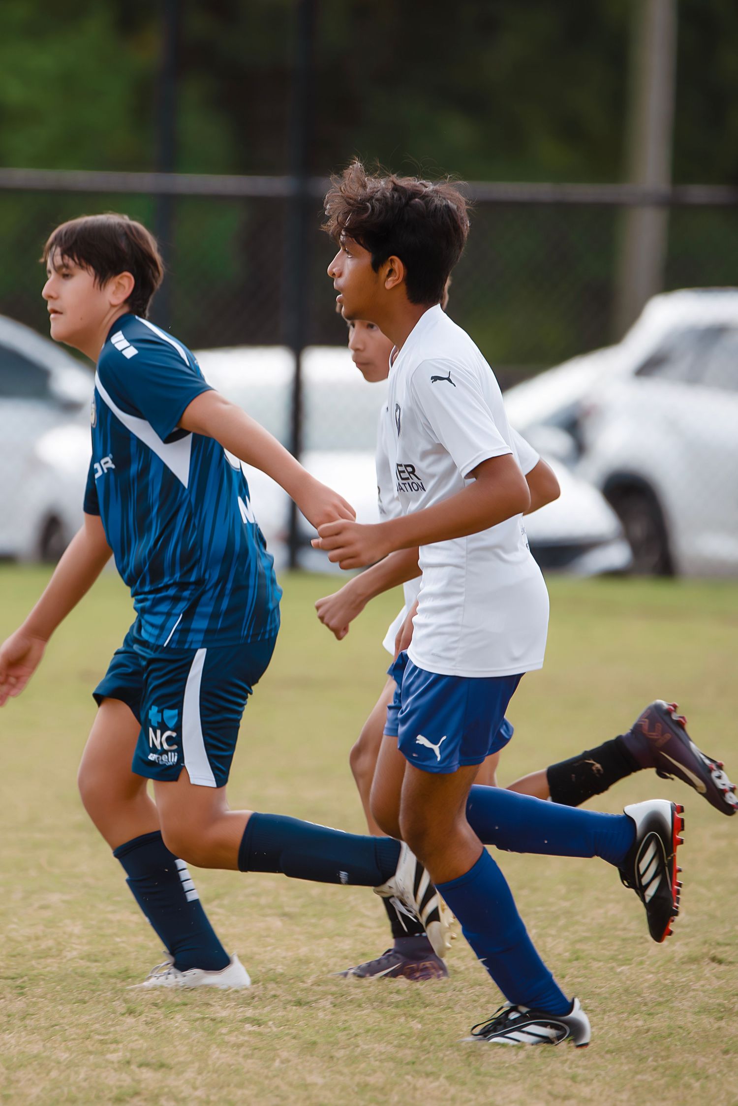Youth soccer players demonstrate jumping and kicking techniques during practice on a grass field.