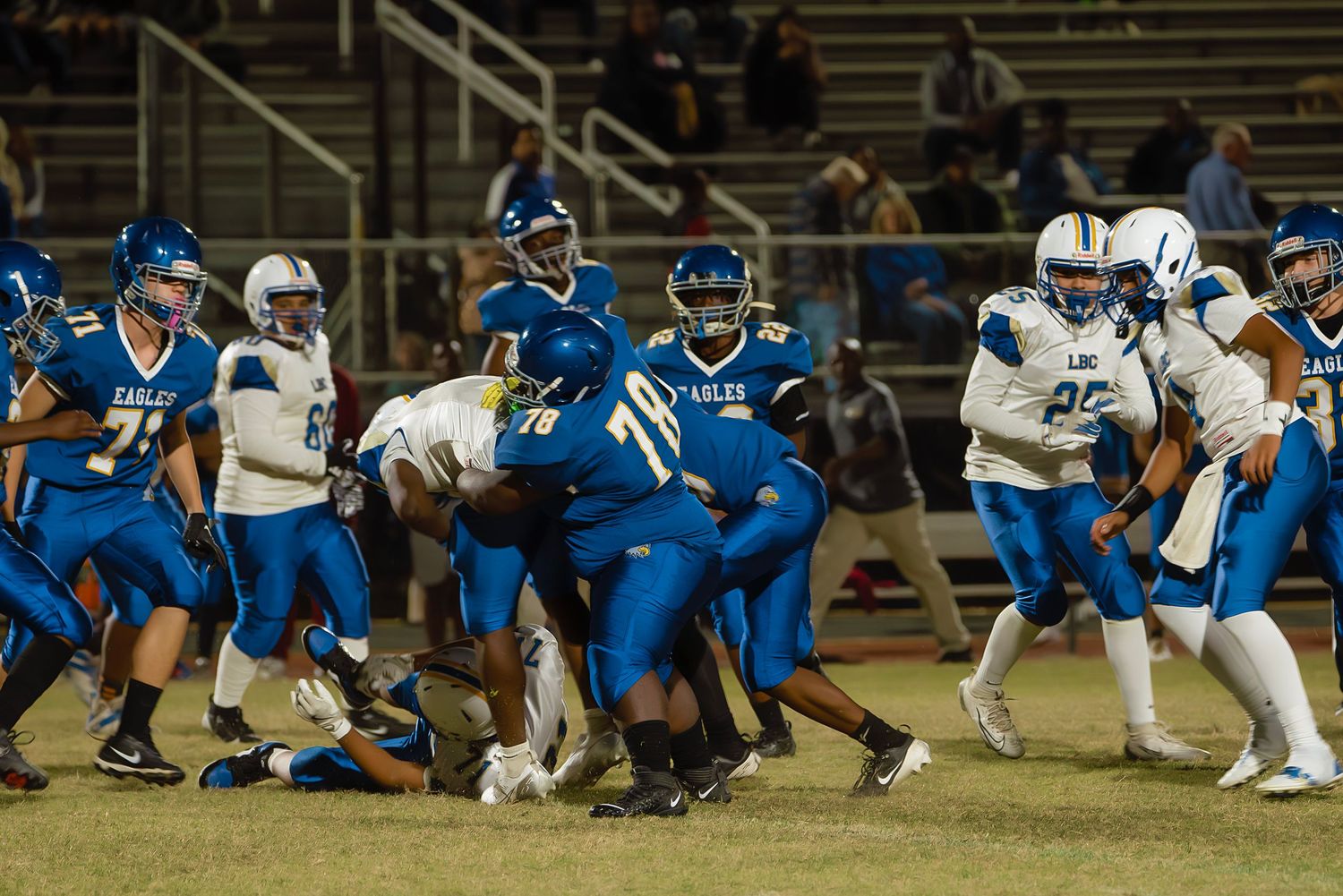 Football players in blue and white uniforms compete during an intense ground play at a night game.