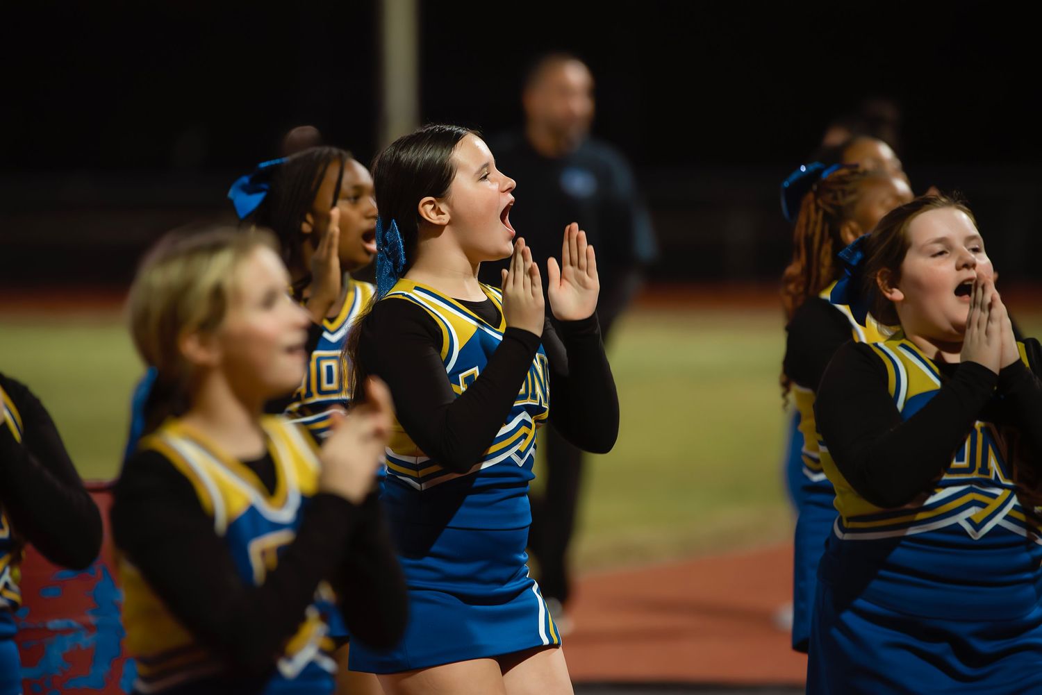 Cheerleaders in blue and yellow uniforms perform energetic routines during a sporting event.