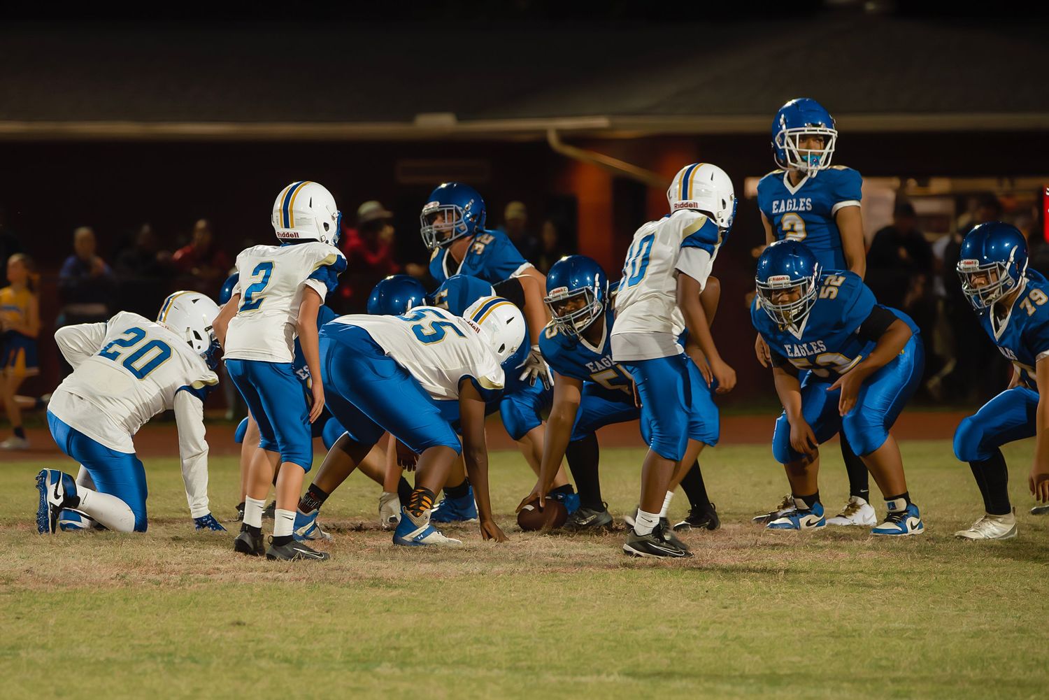 Football players line up at the line of scrimmage during a night game on a grass field.