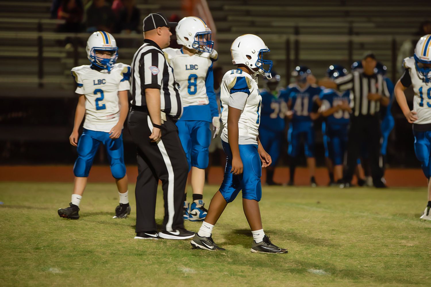 Football players and officials gather on the field during a game with teams in blue and white uniforms.