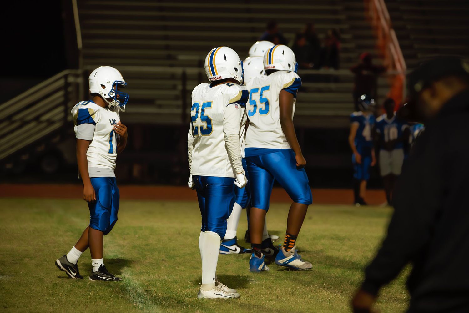 Football players in blue and white uniforms line up on the field during a nighttime game.