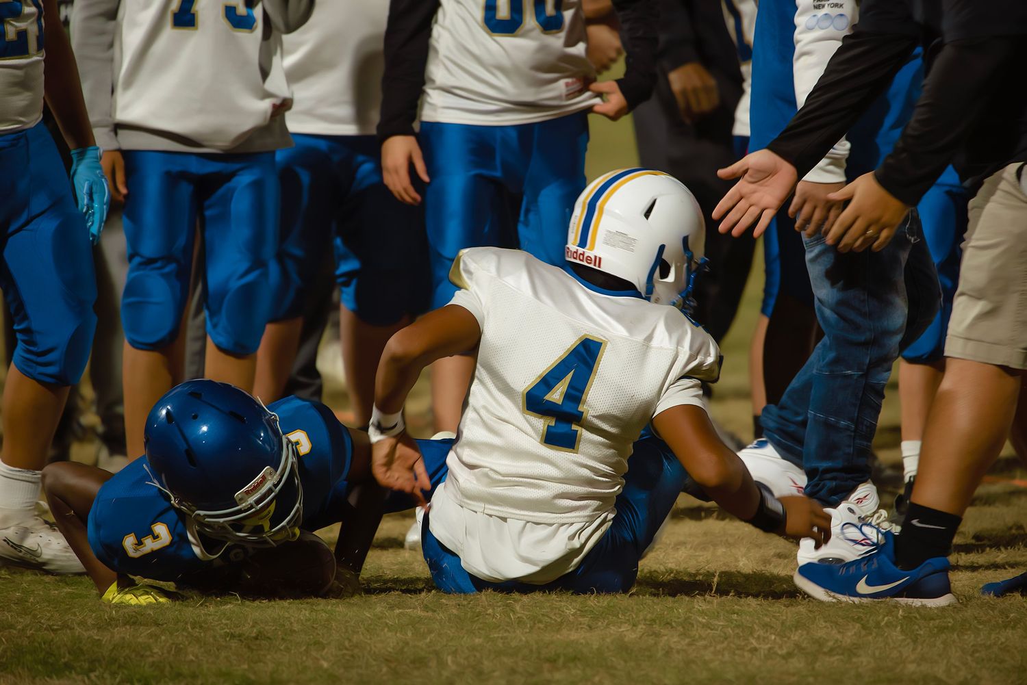 Football players in blue and white uniforms gather on the sidelines during a game.