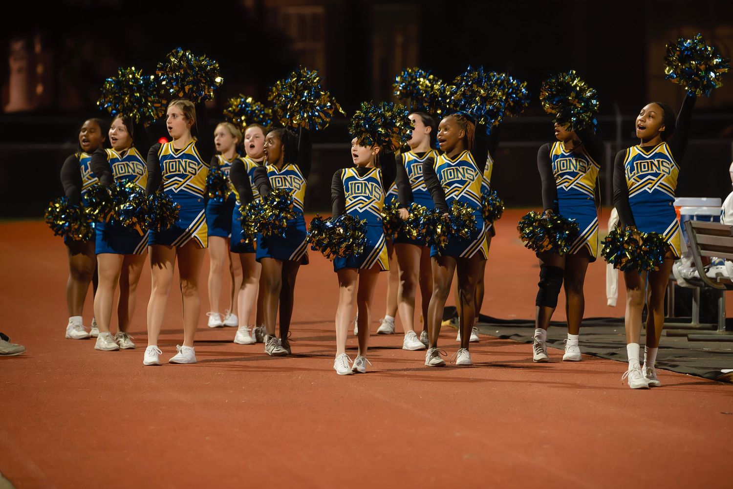 Cheerleaders perform a synchronized routine in formation on a gymnasium floor during a sports event.