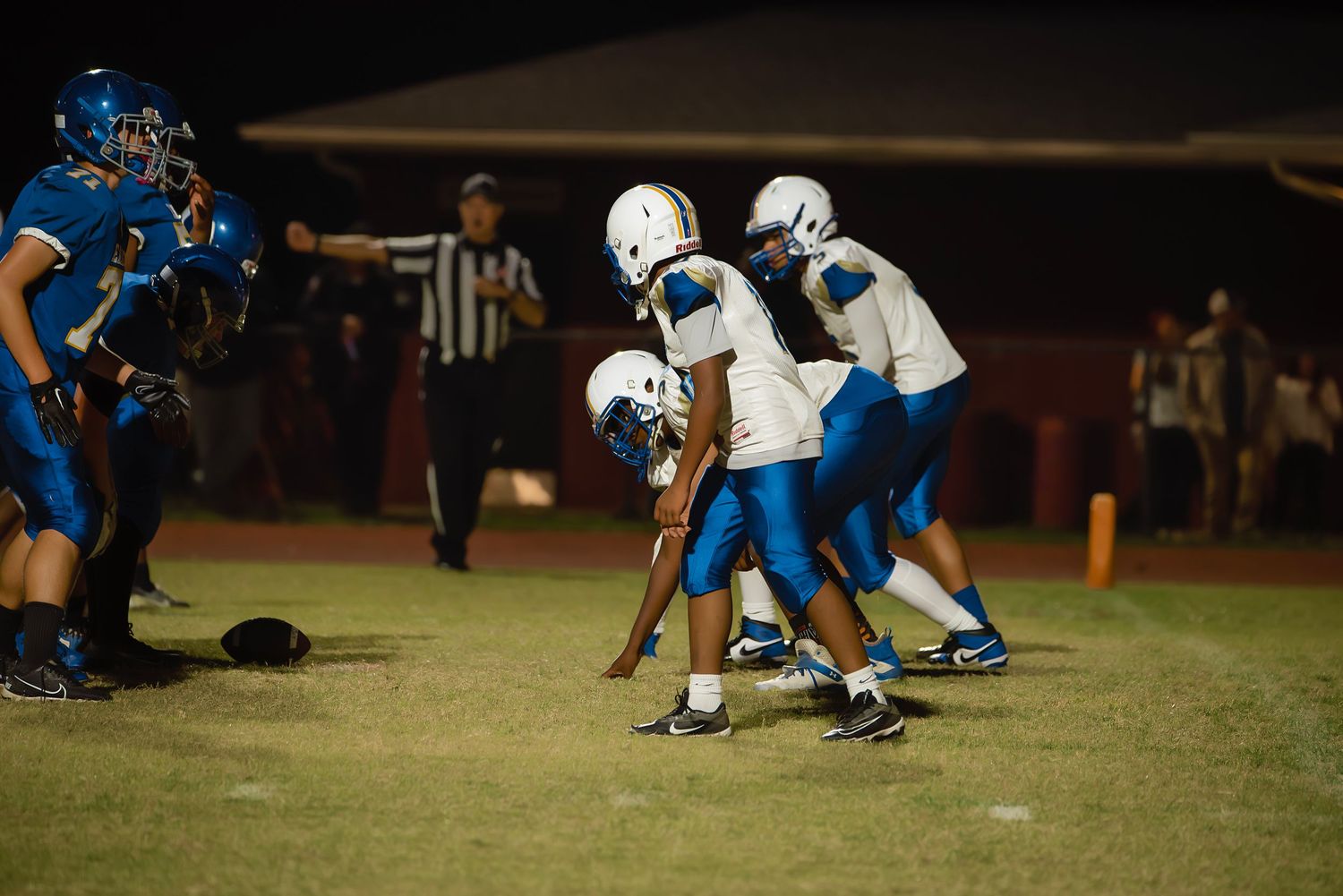 High school football teams face off at the line of scrimmage under stadium lights.