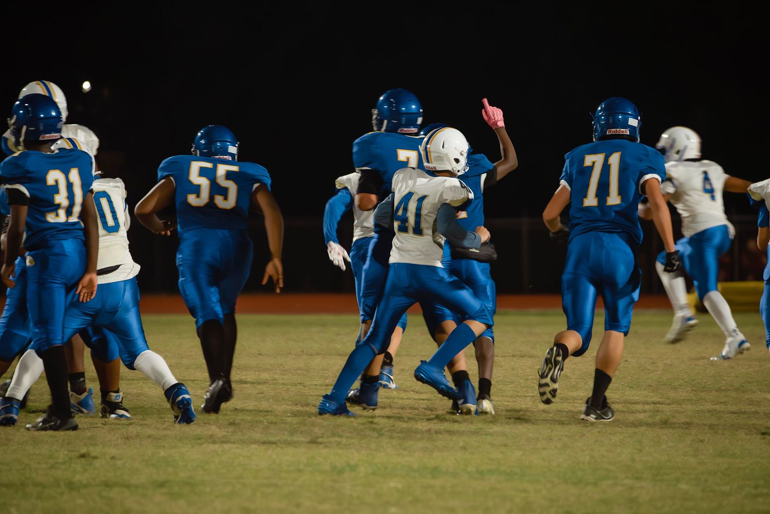 Football players in blue and white jerseys prepare for a play on the field at night.