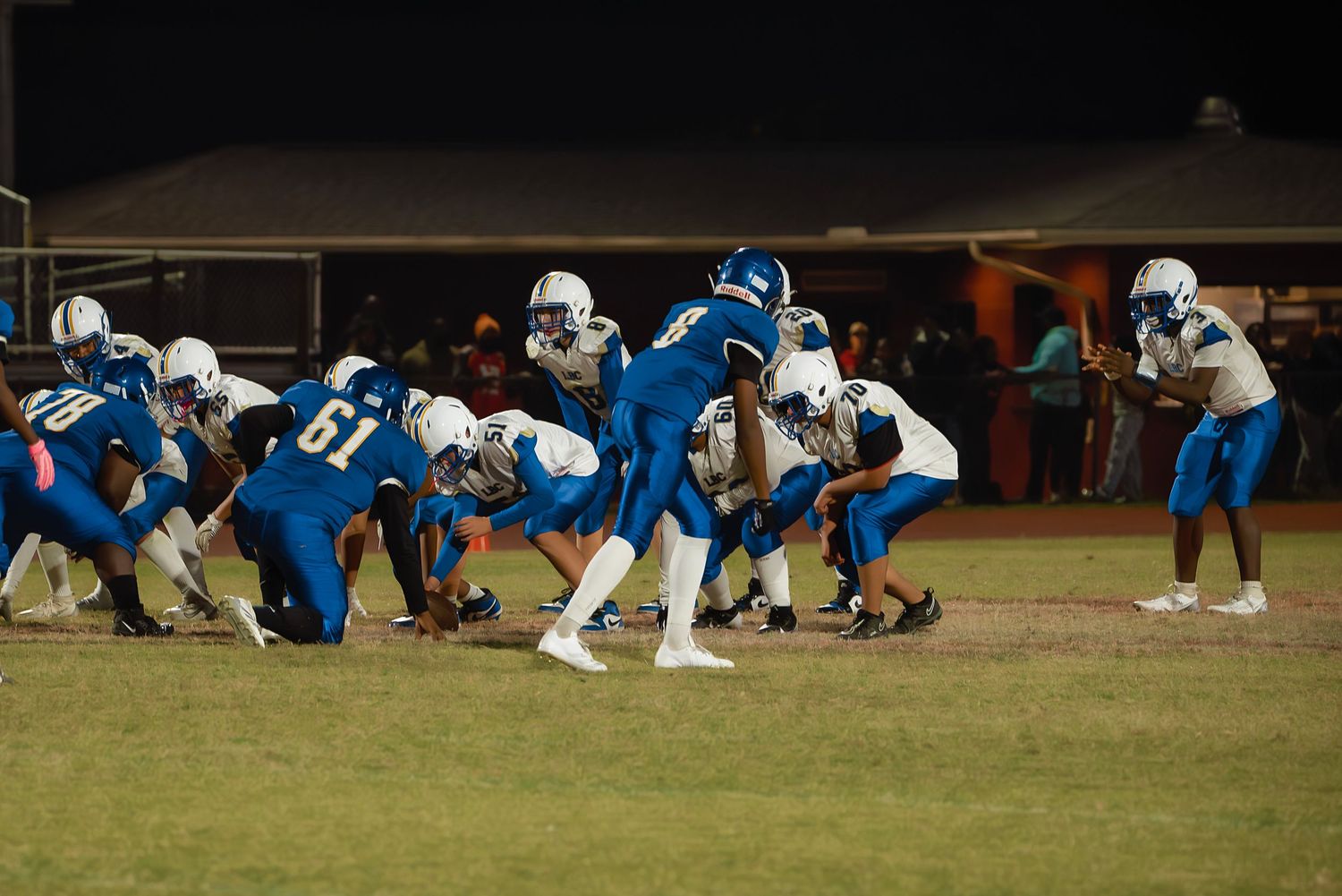 Football players in blue and white uniforms line up in formation on a grass field during a night game.