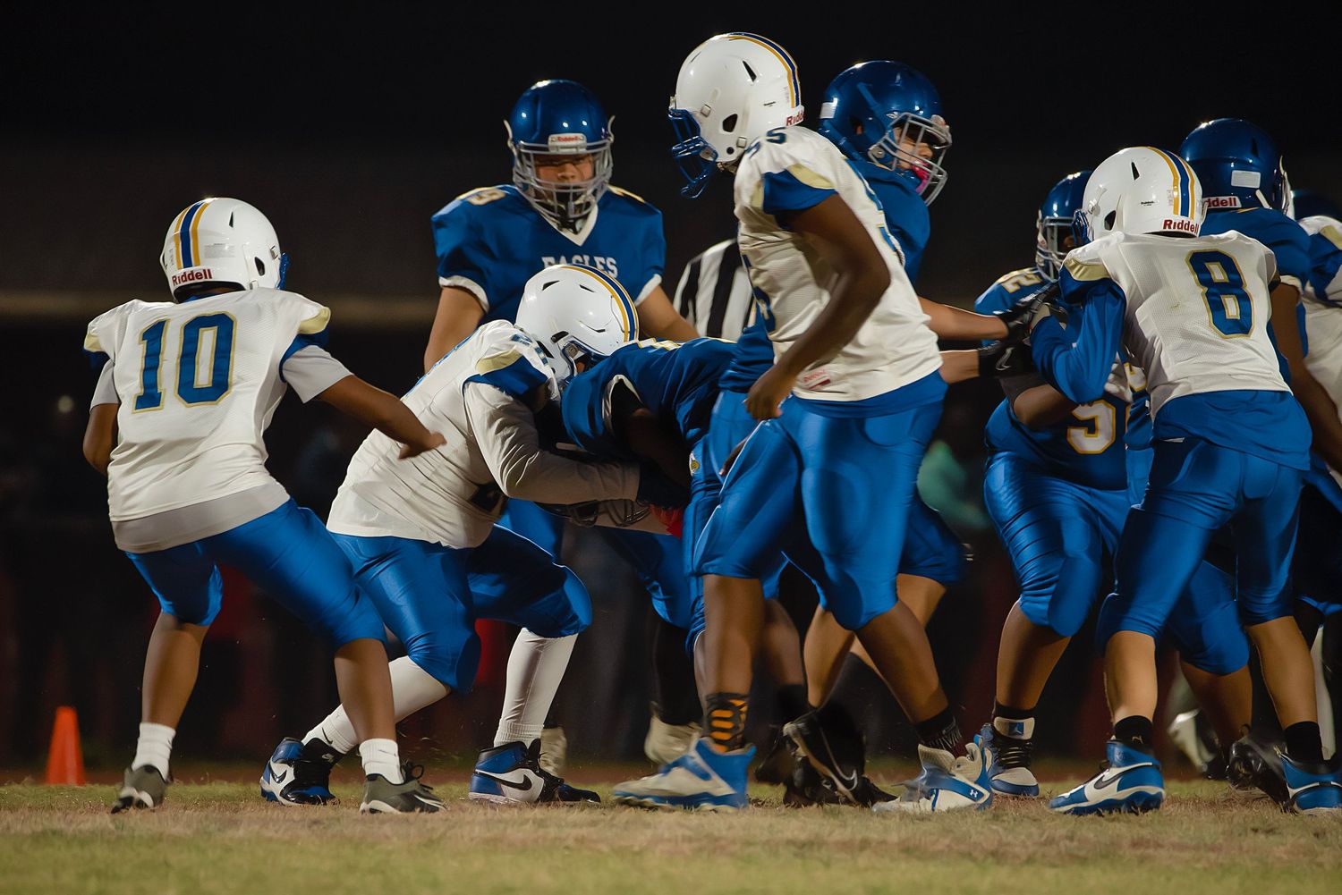 Football players in blue and white uniforms line up for a play during a night game under stadium lights.