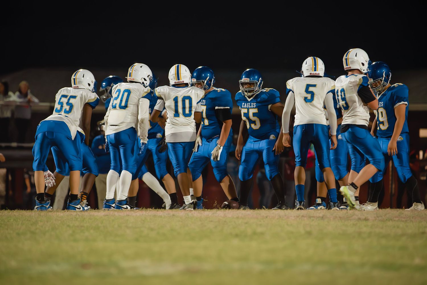 Football players from opposing teams spread across the field during a night game.